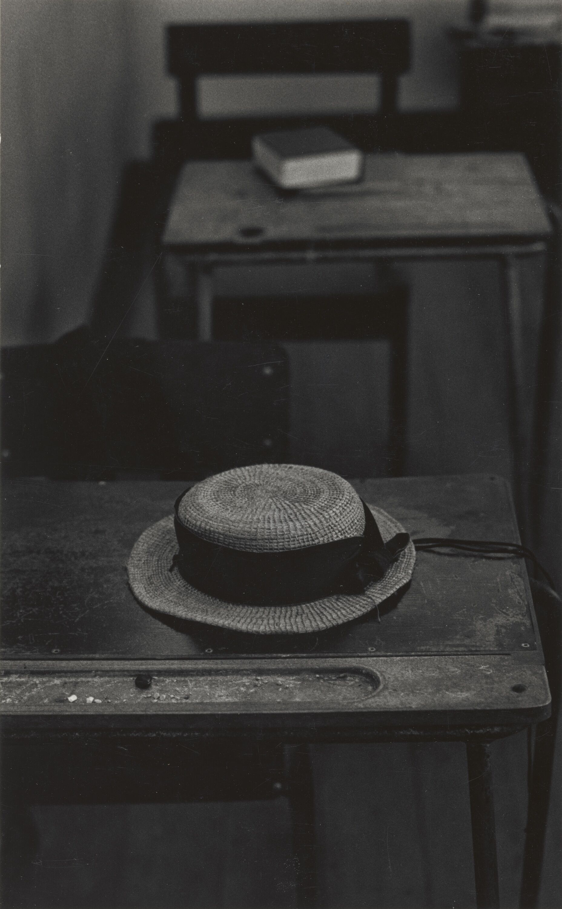 A hat with ribbon above its brim, rested on top of a child's school desk.