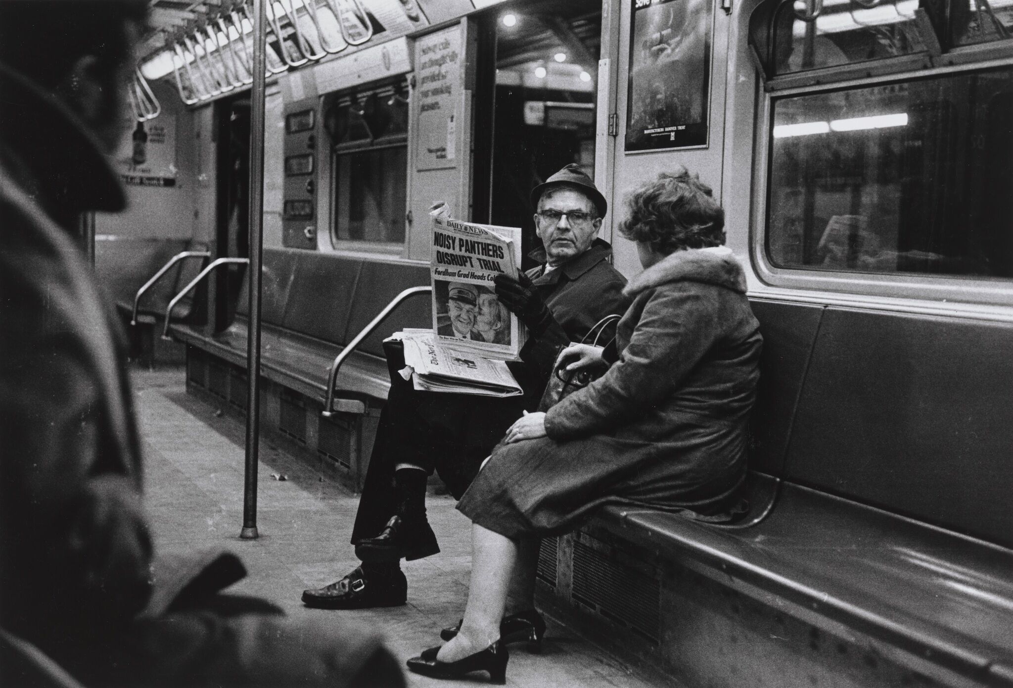 Two people sitting inside a subway talking to one another.