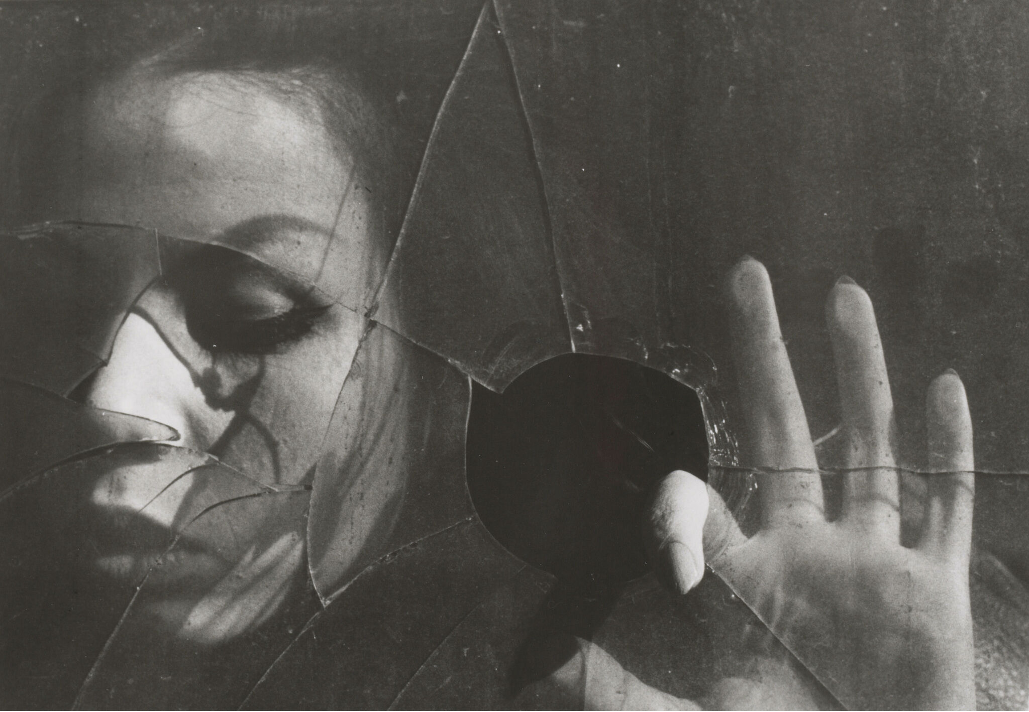 A close-up of a woman's face behind broken glass. 