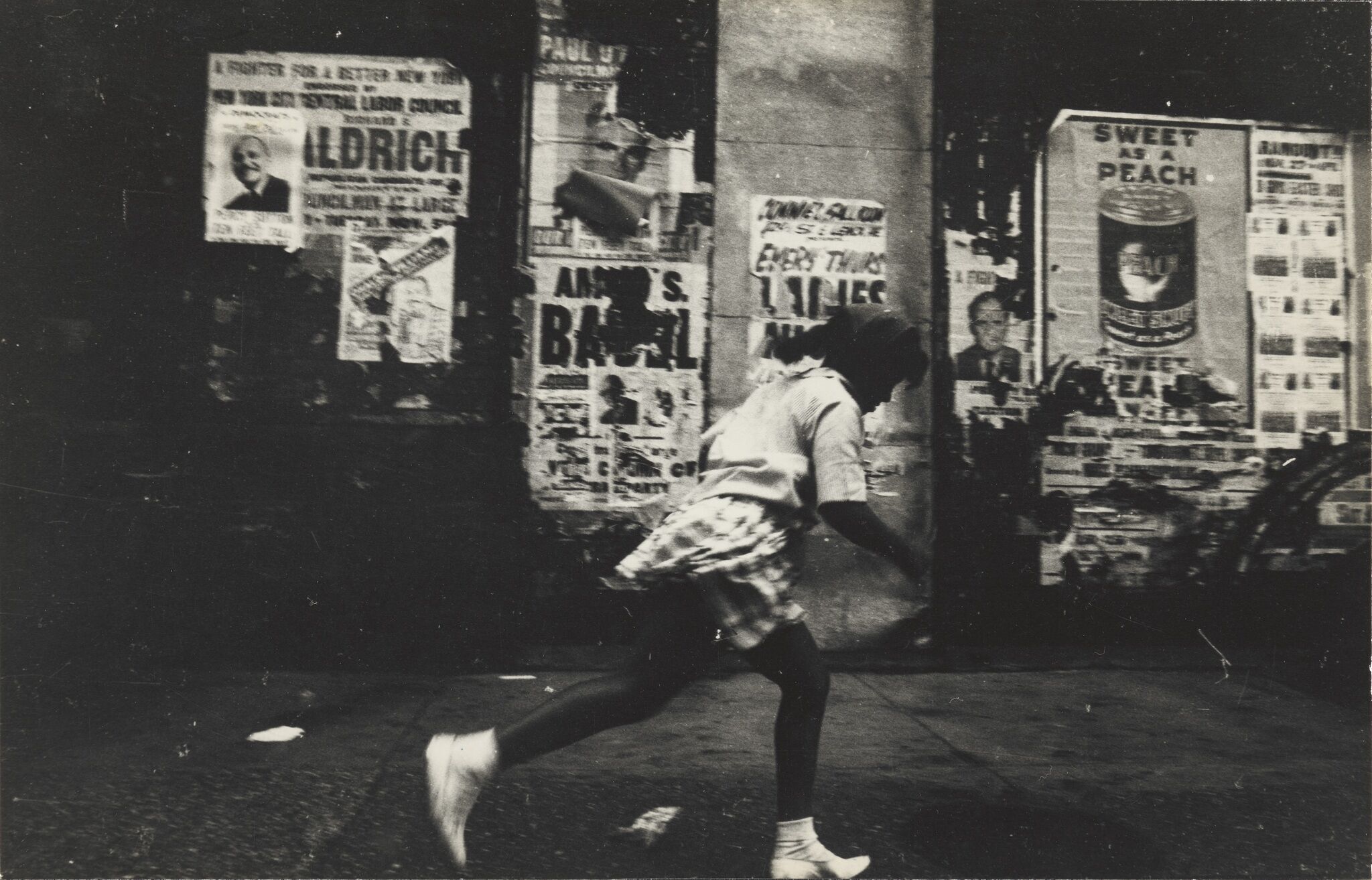 A girl running on a street with print advertisements pasted on the wall next to her.