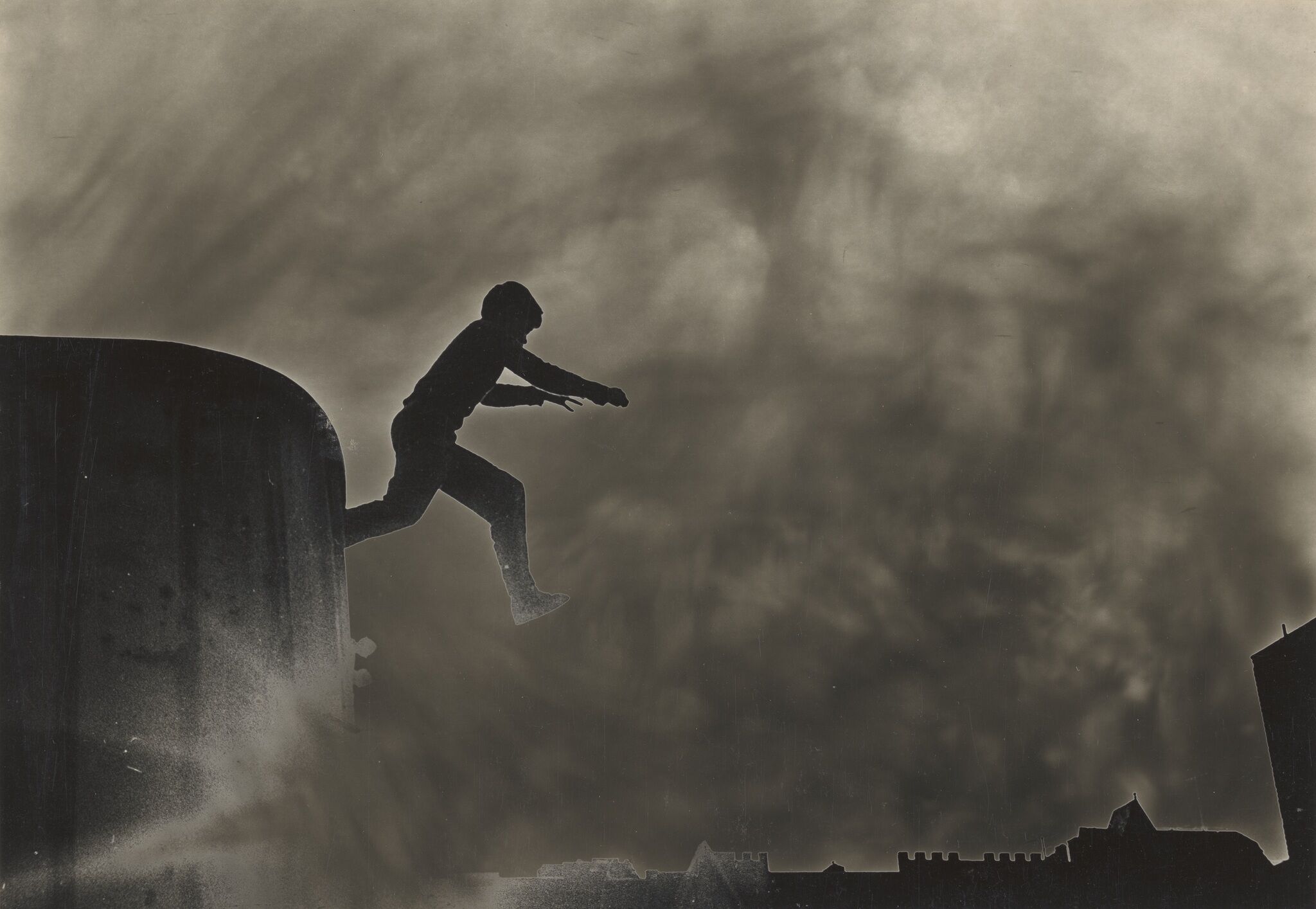 A silhouette of a person jumping down from a building with a silhouette of other buildings in the background.