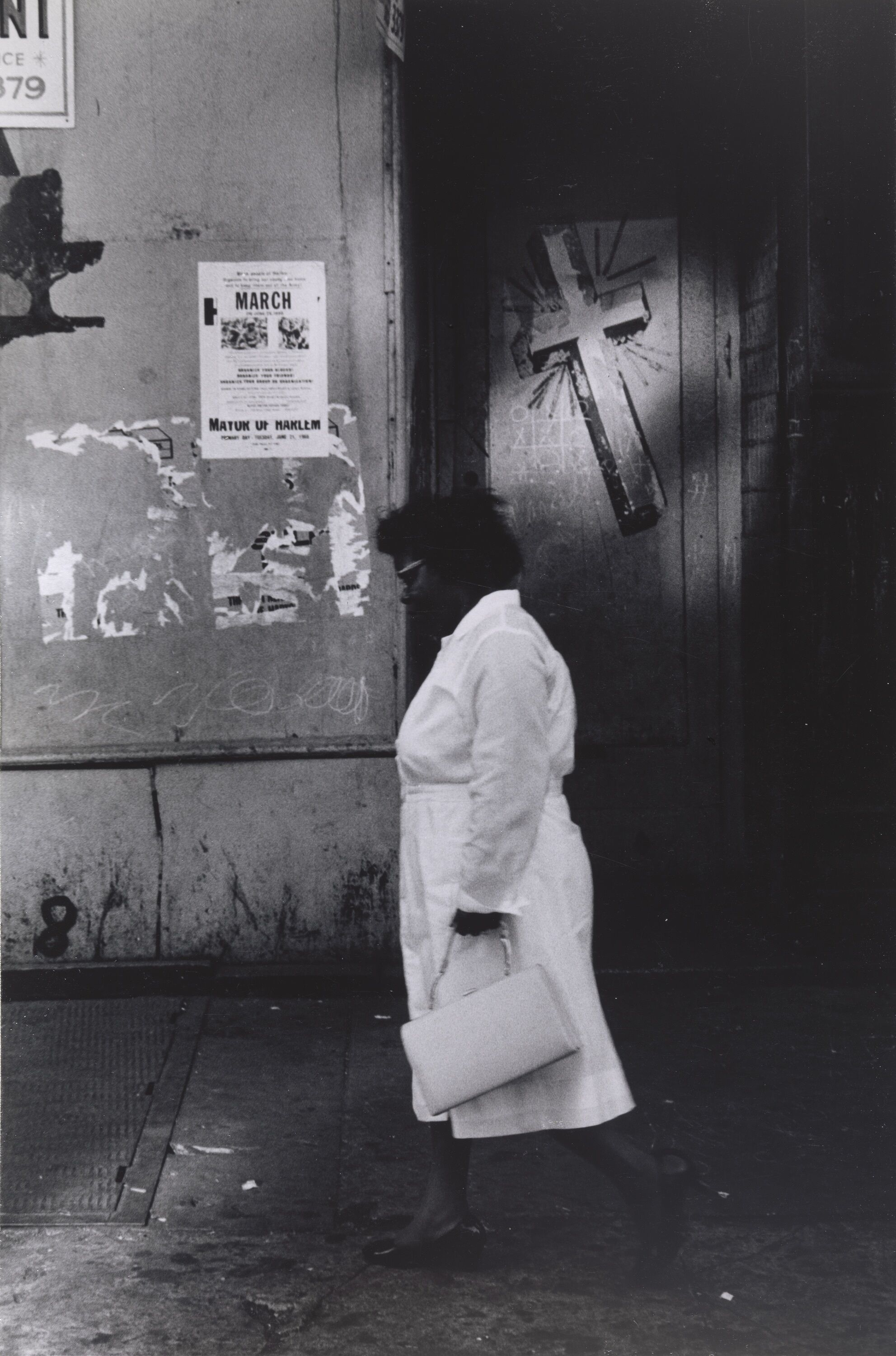 A woman walking down a street, wearing a white dress and holding a handbag.