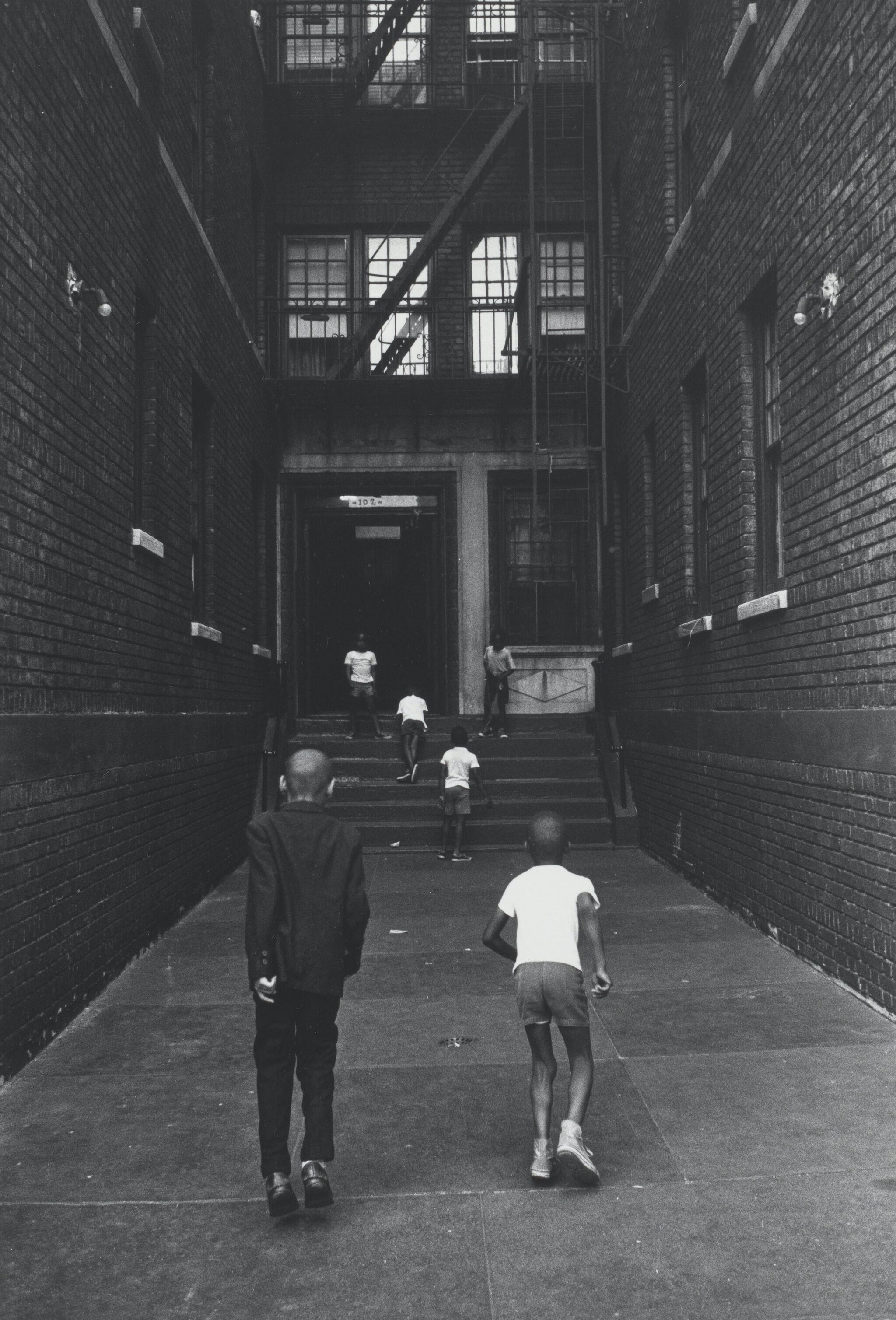 Two people in an alley walking away from the camera. 