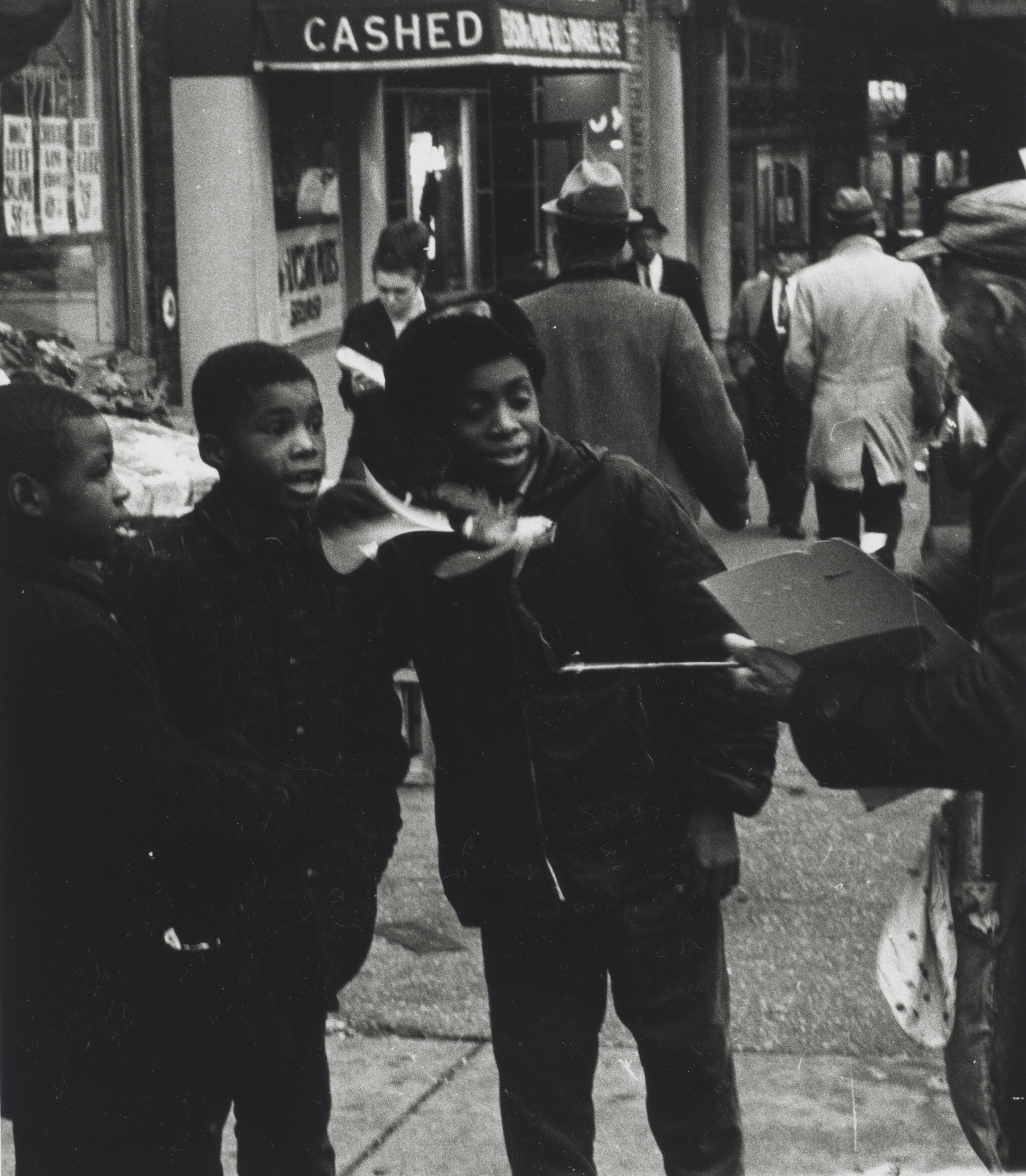 Three boys on the sidewalk facing someone to their right. 