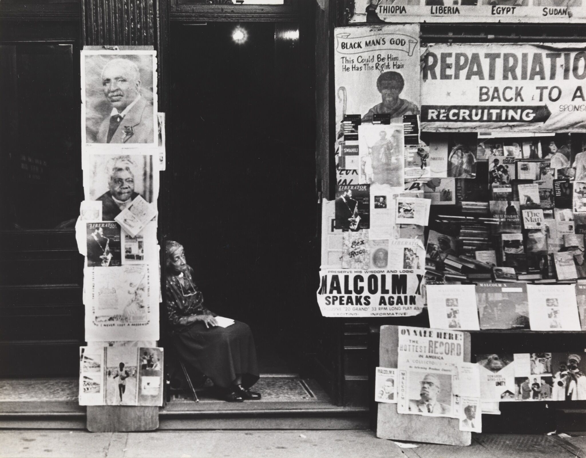 A woman sitting in front of a doorway next to a building covered with posters.