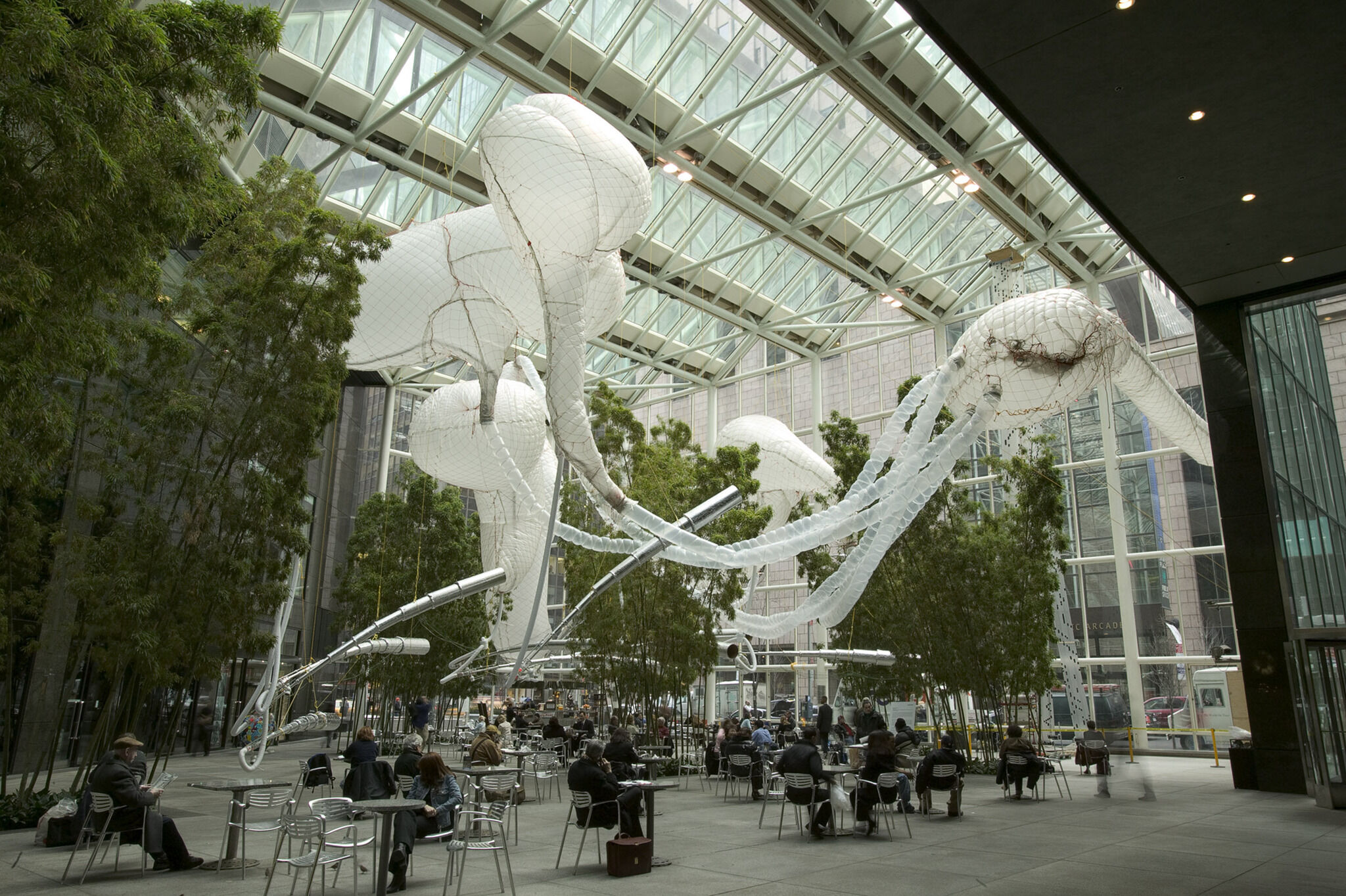A large white sculpture displayed above people alongside trees.