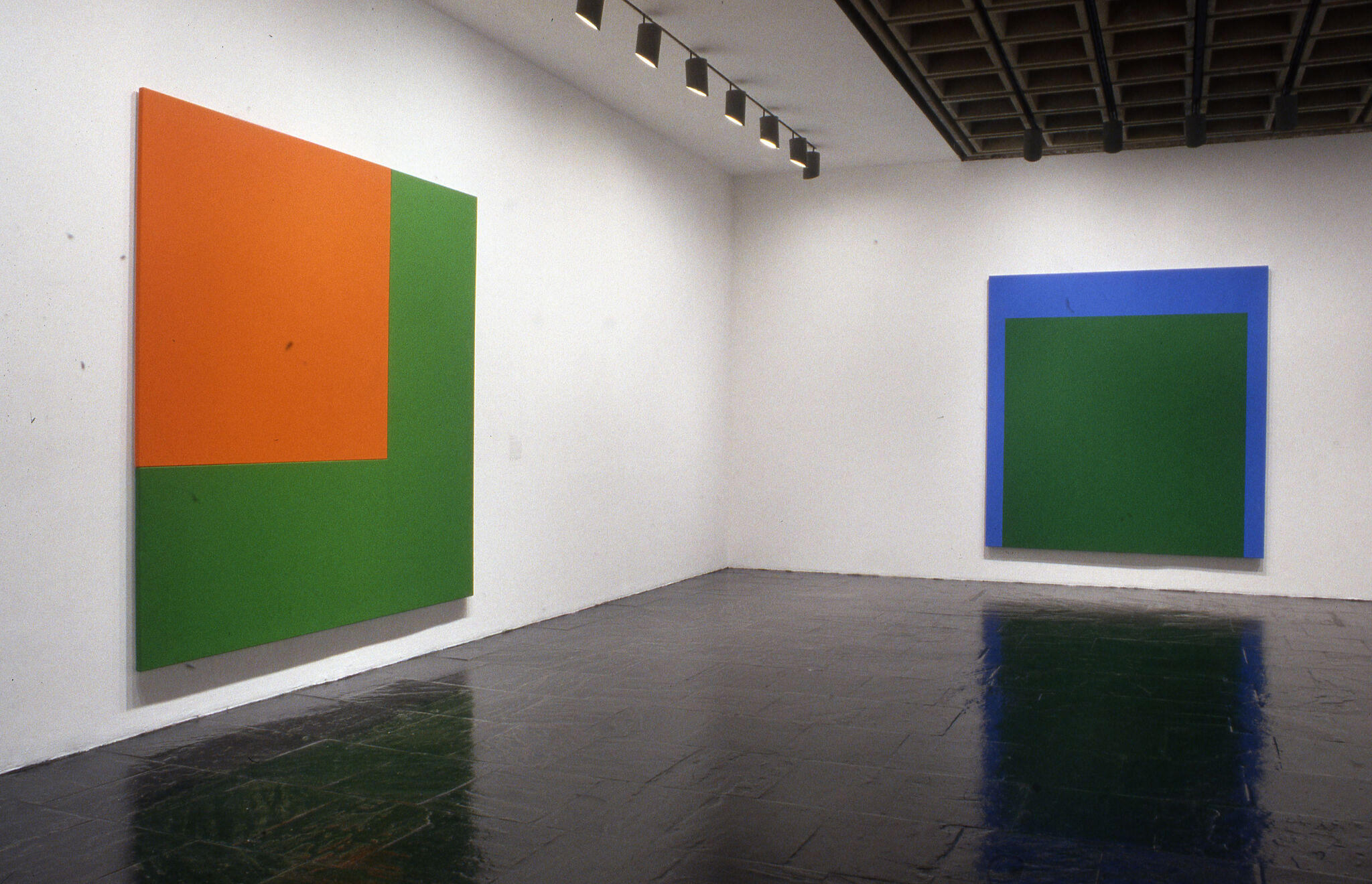 Two large square abstract paintings displayed on the walls of a gallery.