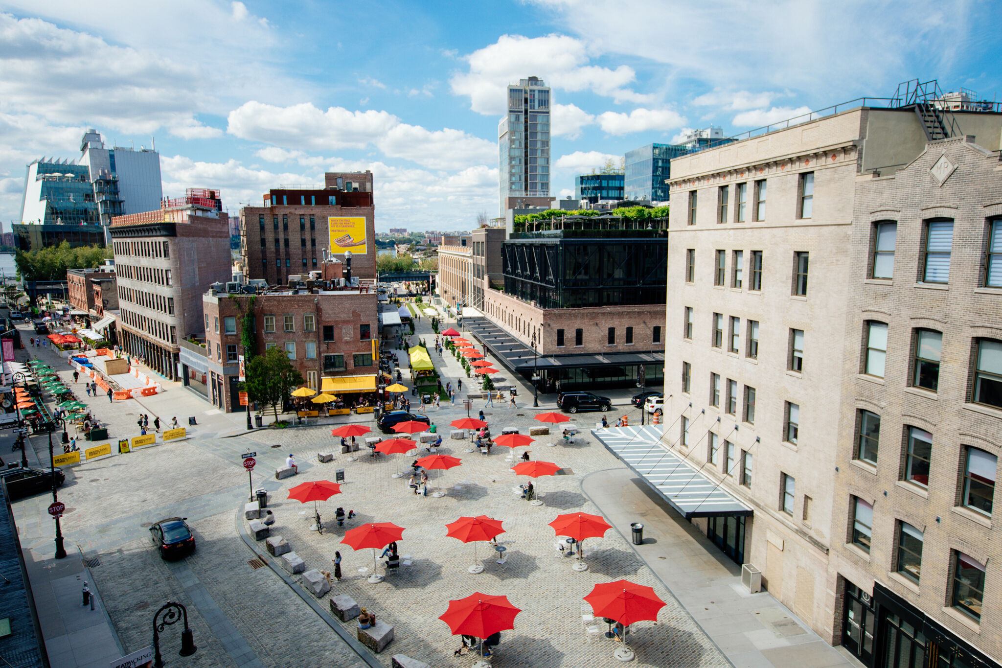 A series of buildings surround the open Gansevoort Plaza, which features a series of open-seating tables with red umbrellas.