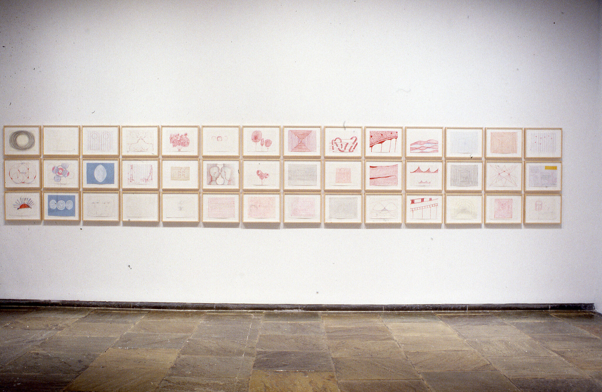 Three rows of drawings displayed in frames hung on a wall.