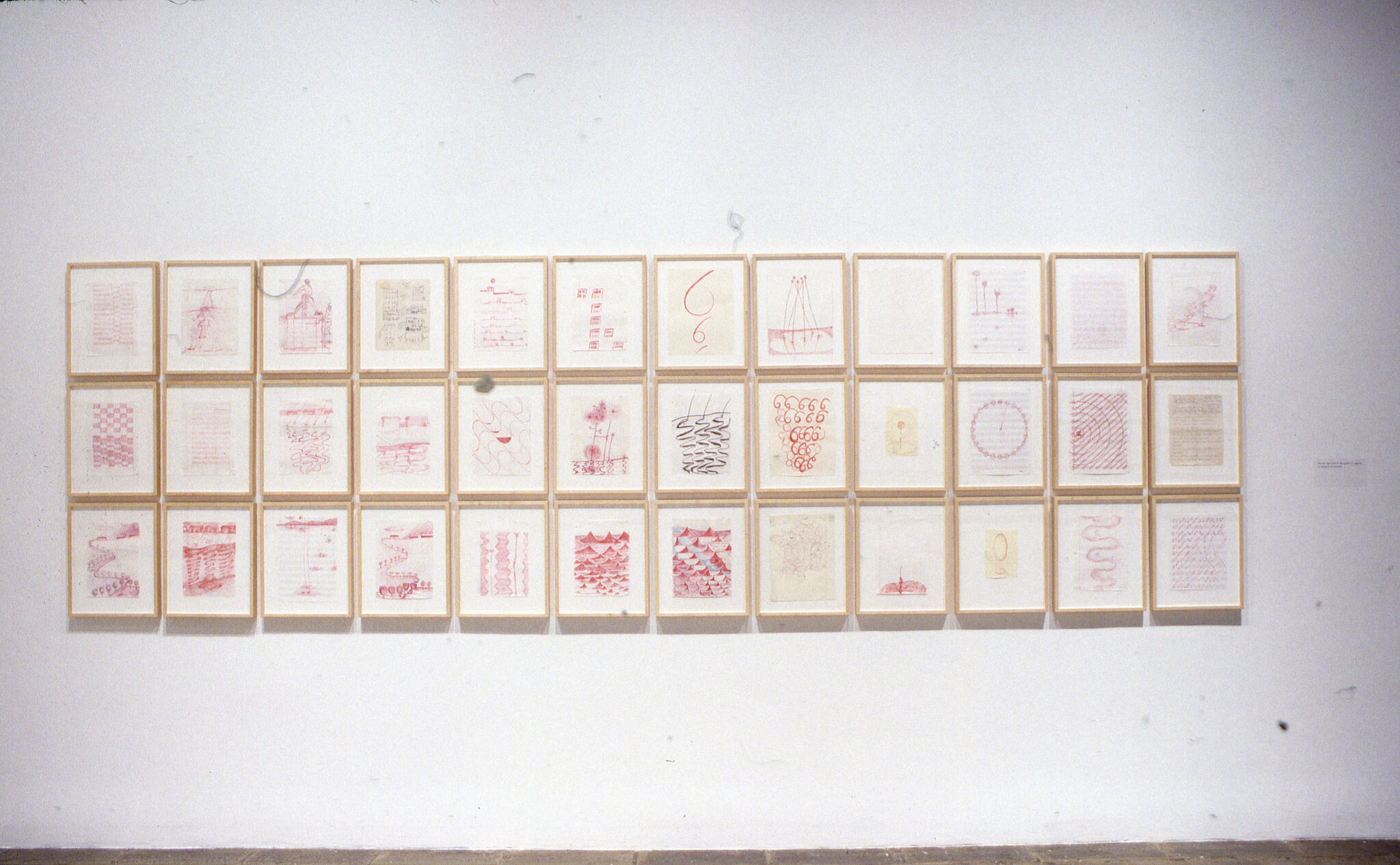 Three rows of drawings displayed in frames hung on a wall.