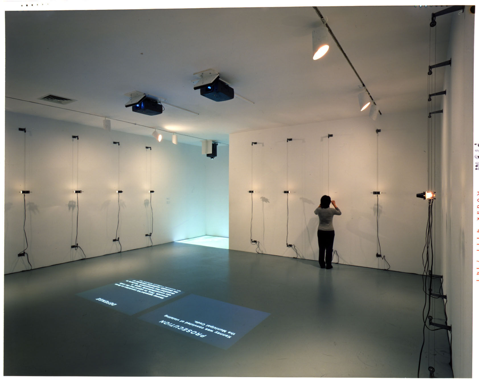 A gallery with two projectors on the ceiling projecting text on the ground.