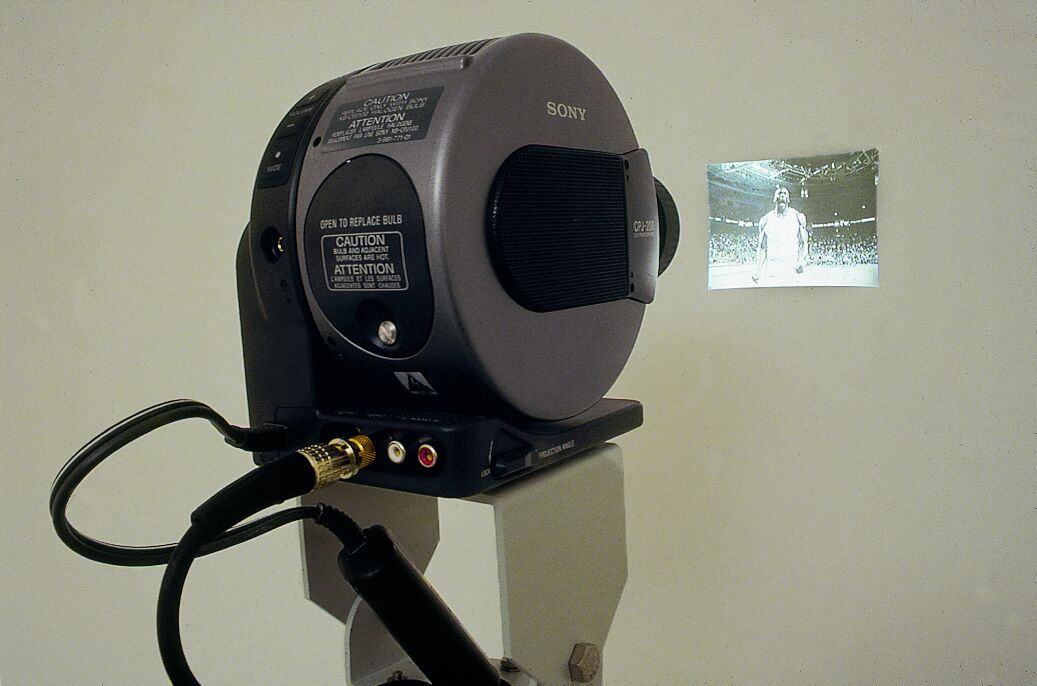 A projector projecting a small black and white view of a figure on a wall.