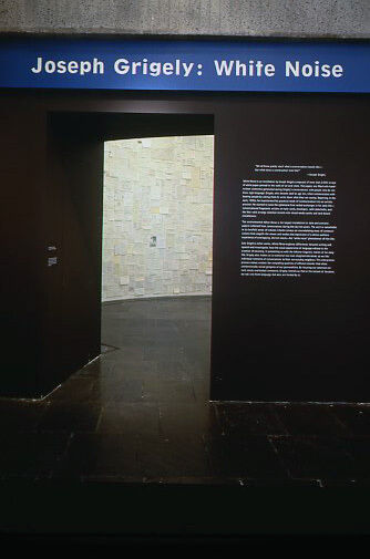 The entrance to Joseph Grigely: White Noise, with black walls and white wall text.