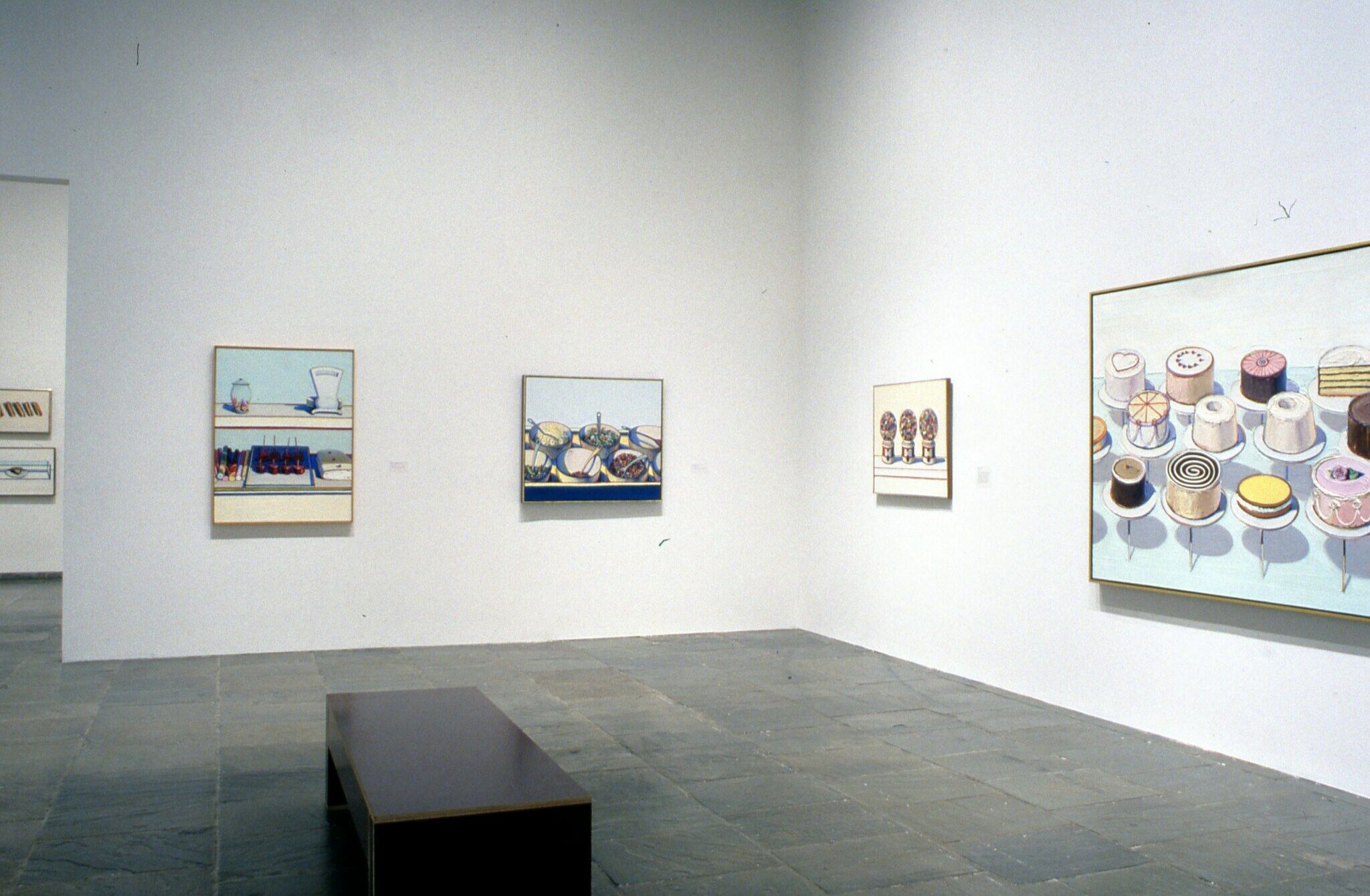 Paintings of food, including cakes, gumball machines, salads, and sweets, displayed in a gallery.