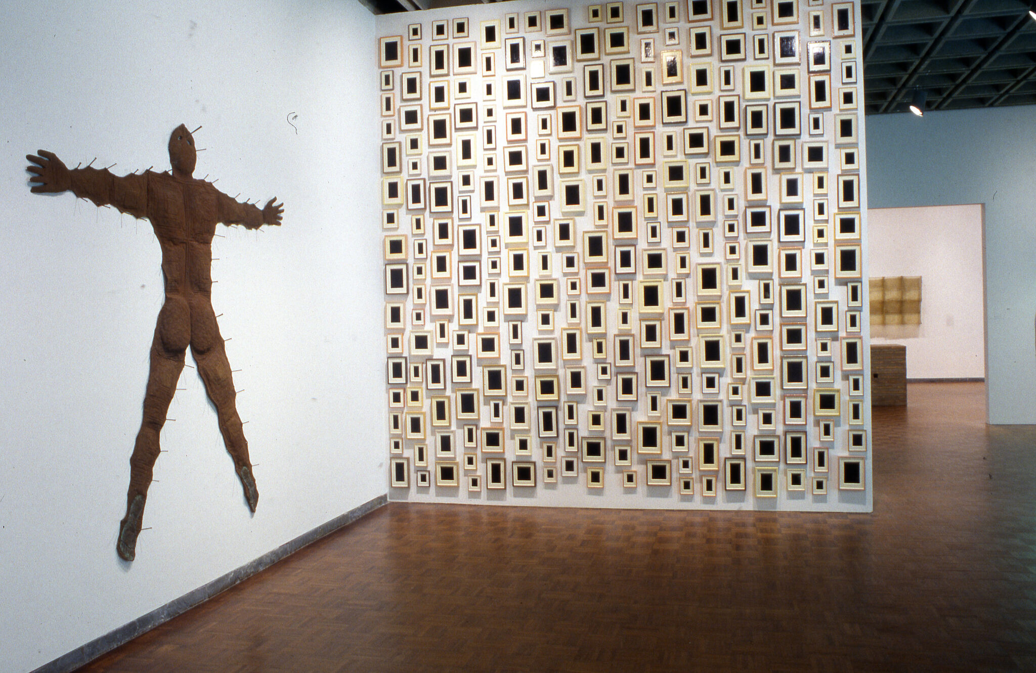 A brown sculpture of a figure displayed against a wall, next to another wall completely covered in small picture frames.