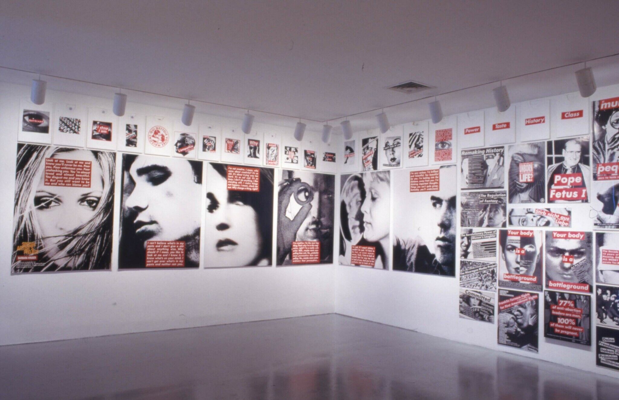 A corner of a gallery covered with black and white photographs that are overlaid with white text highlighted in red.