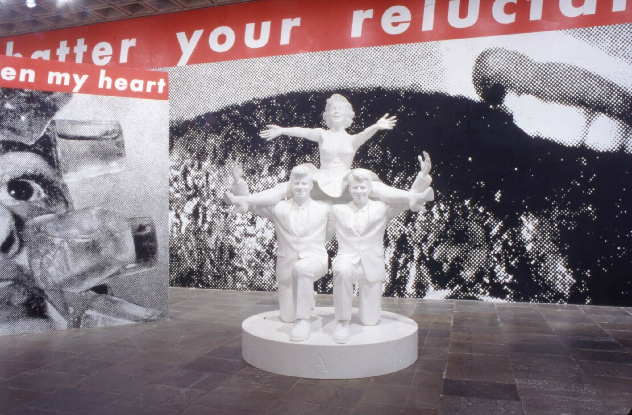 A white sculpture of two men down on their knee with a woman on their shoulders.