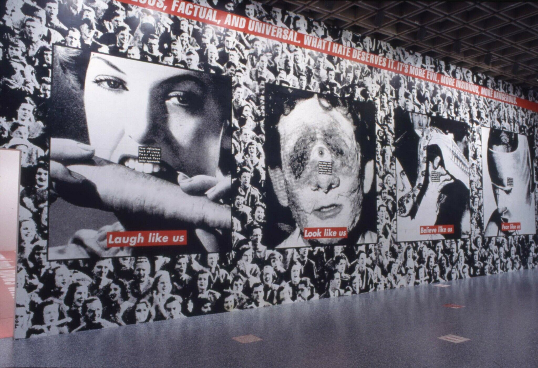 A wall in a gallery covered with a black and white photograph of a crowd, along with other photos displayed on the wall.