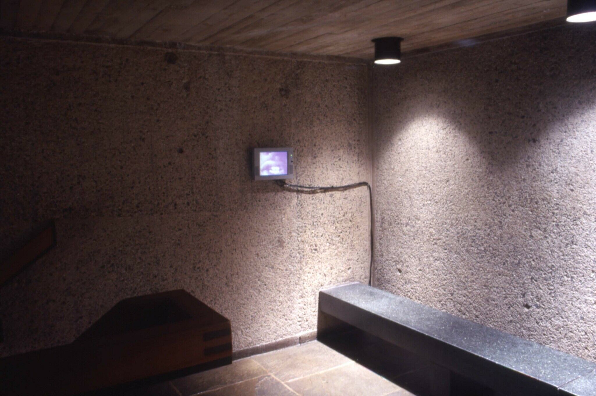 A dimly lit gallery space with a small monitor on a wall.