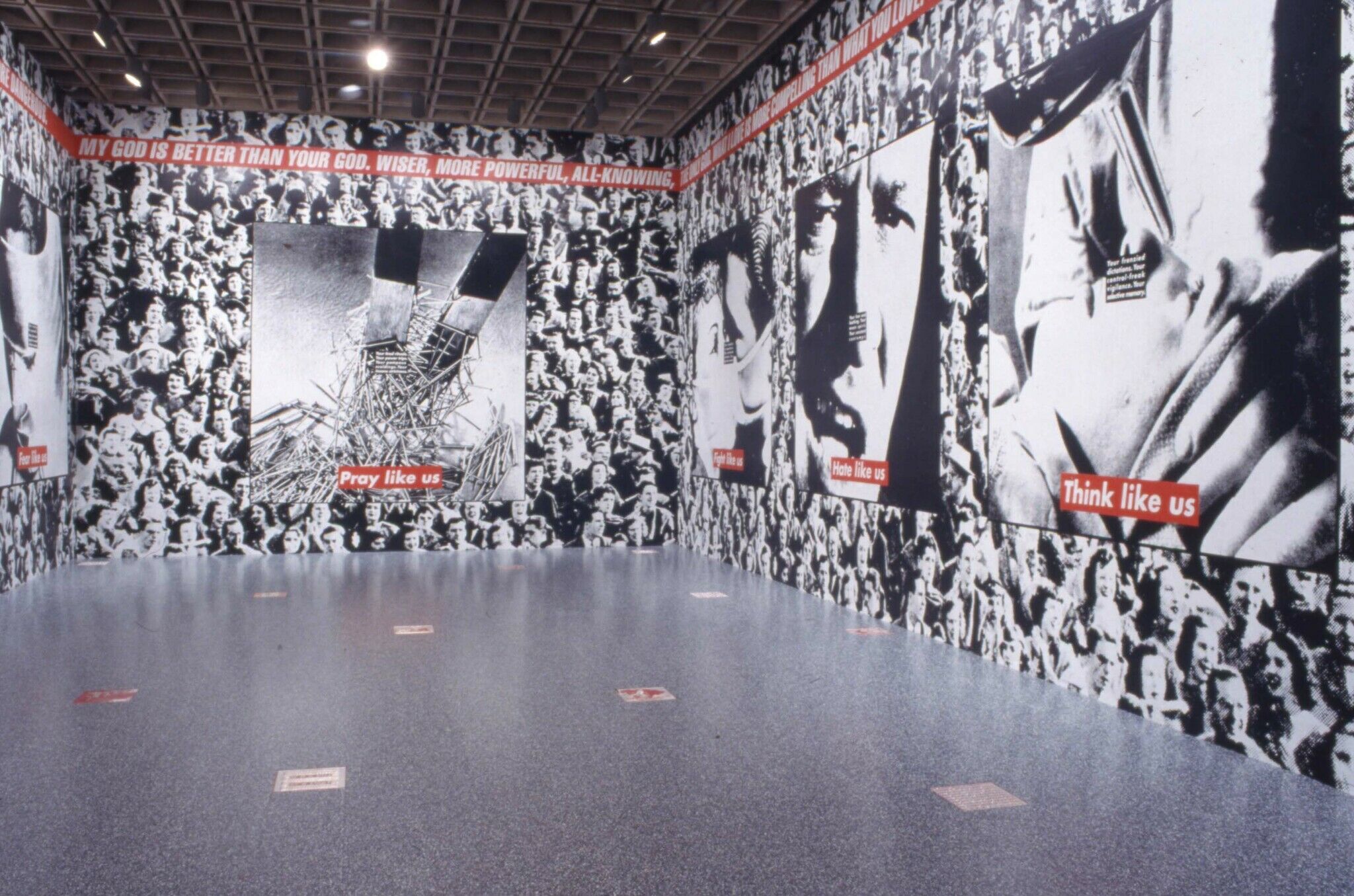 A gallery with walls covered in a black and white photograph of a crowd, along with other works of art displayed on the walls.