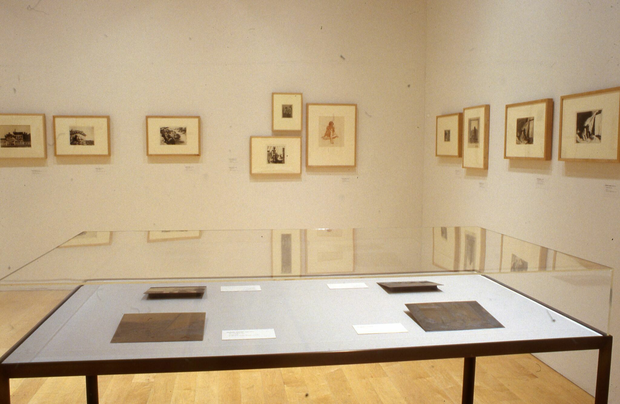 A gallery with prints displayed on the walls and in a display case on a tabletop.