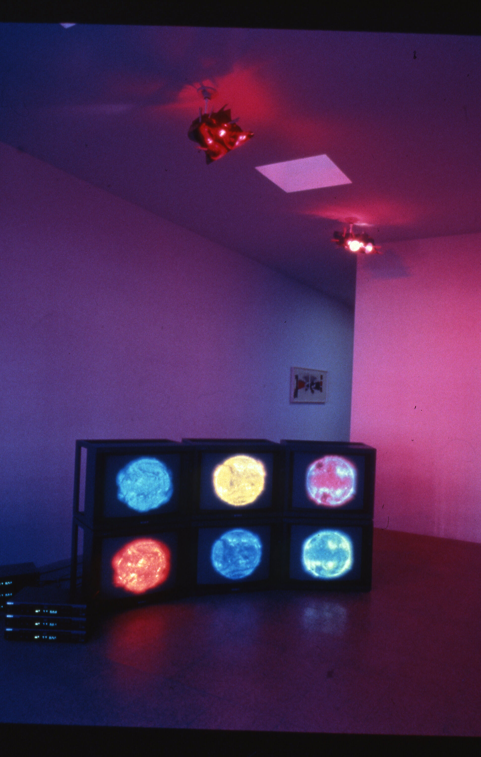 A gallery lit in blue and red hued lights, along with six monitors each displaying a colored circle.