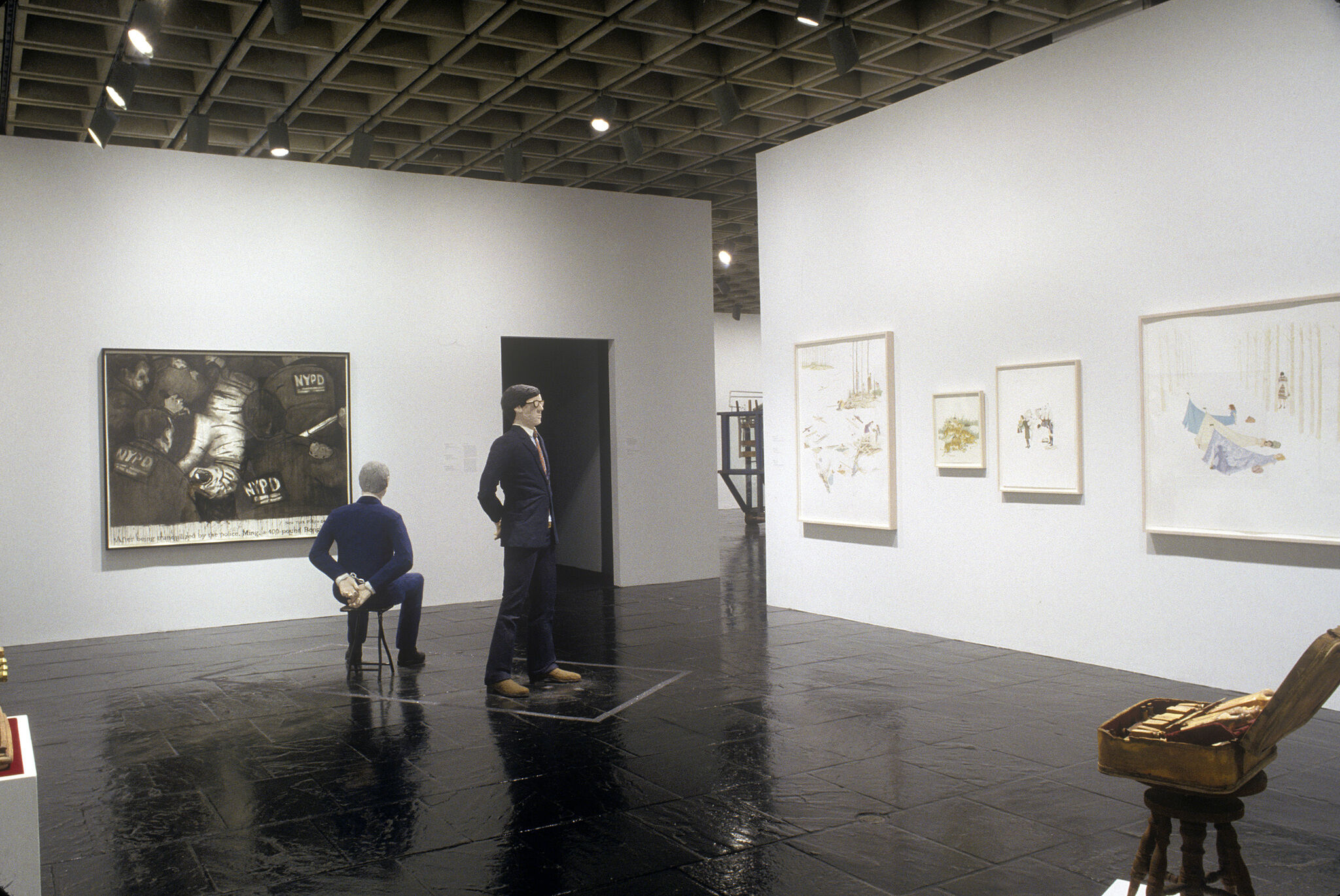 A gallery filled with prints and a sculpture of a man standing and another sculpture of a man sitting.