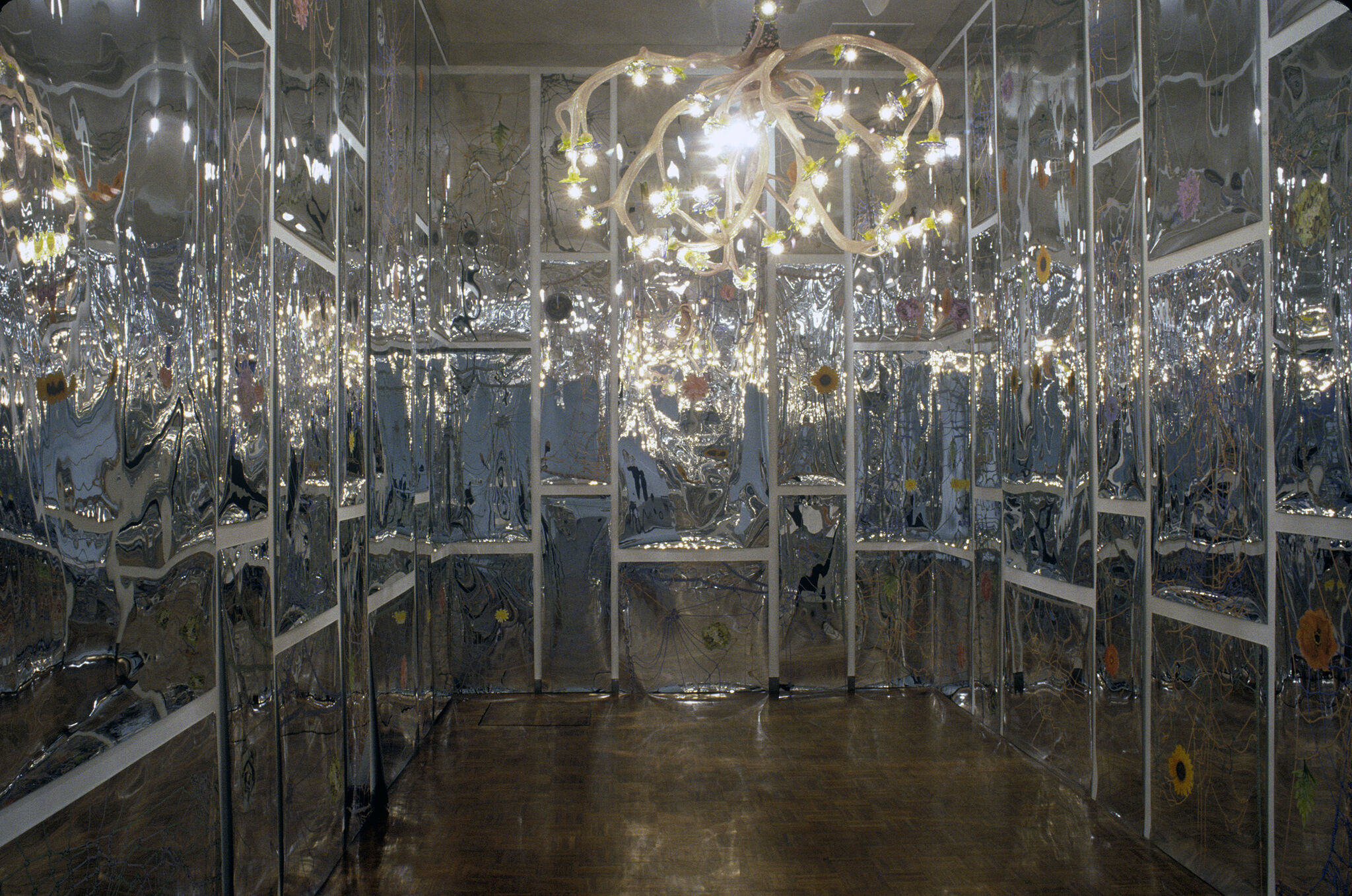 A mixed media installation of a room with walls covered in reflective material and a chandelier.