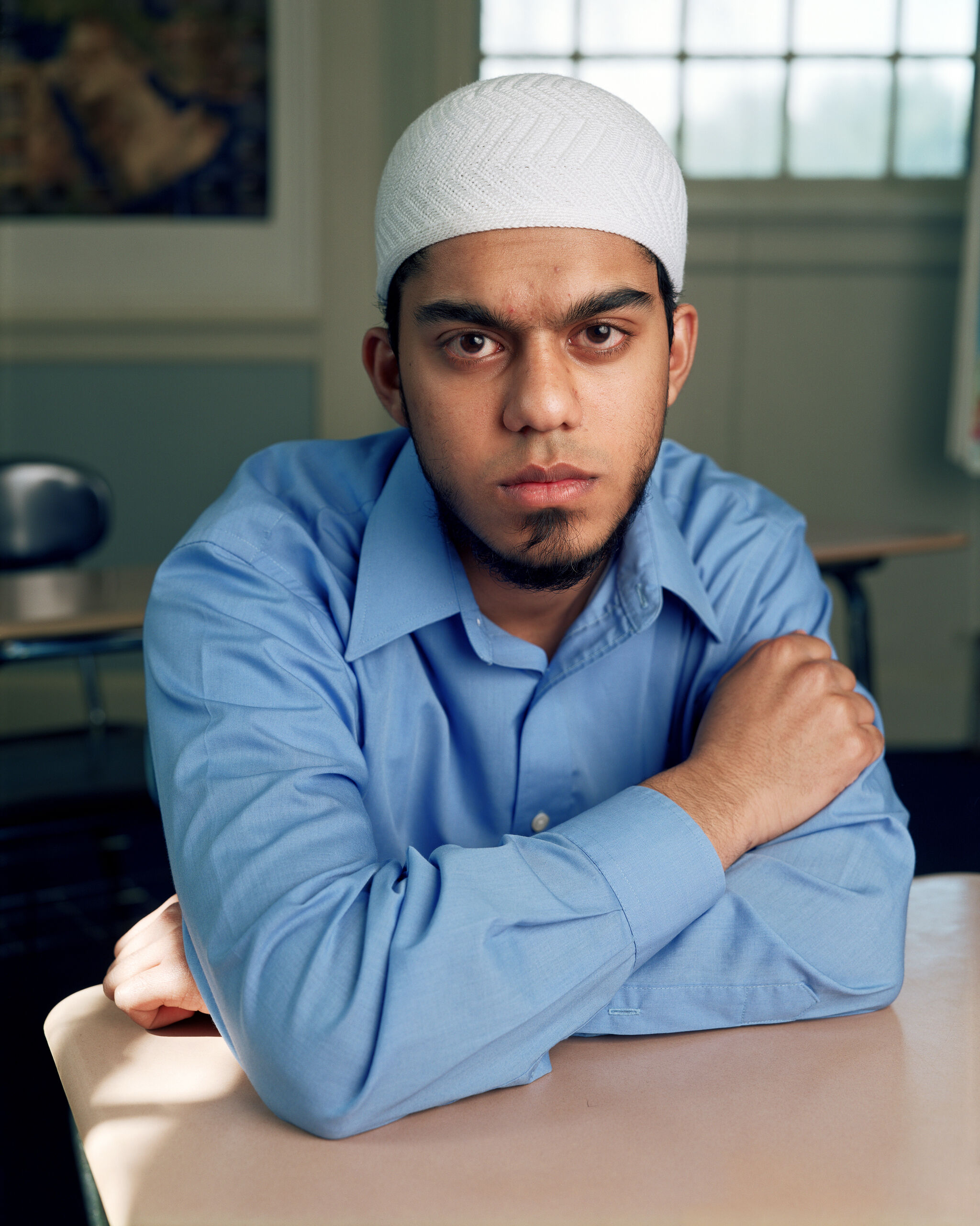 A portrait of a young student with their arms resting against a school desk. 