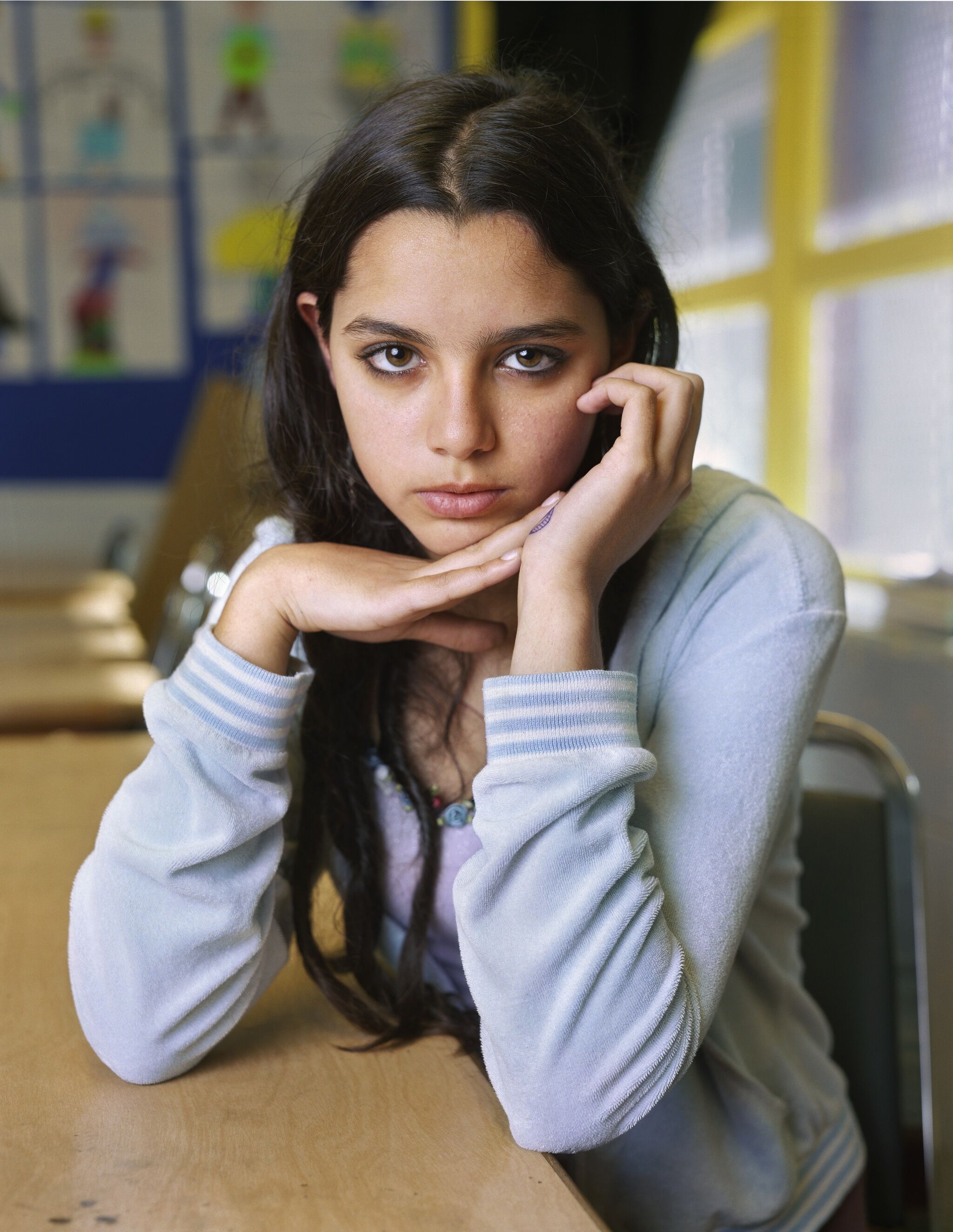 A portrait of a student resting their arms on a school desk and facing the camera. 