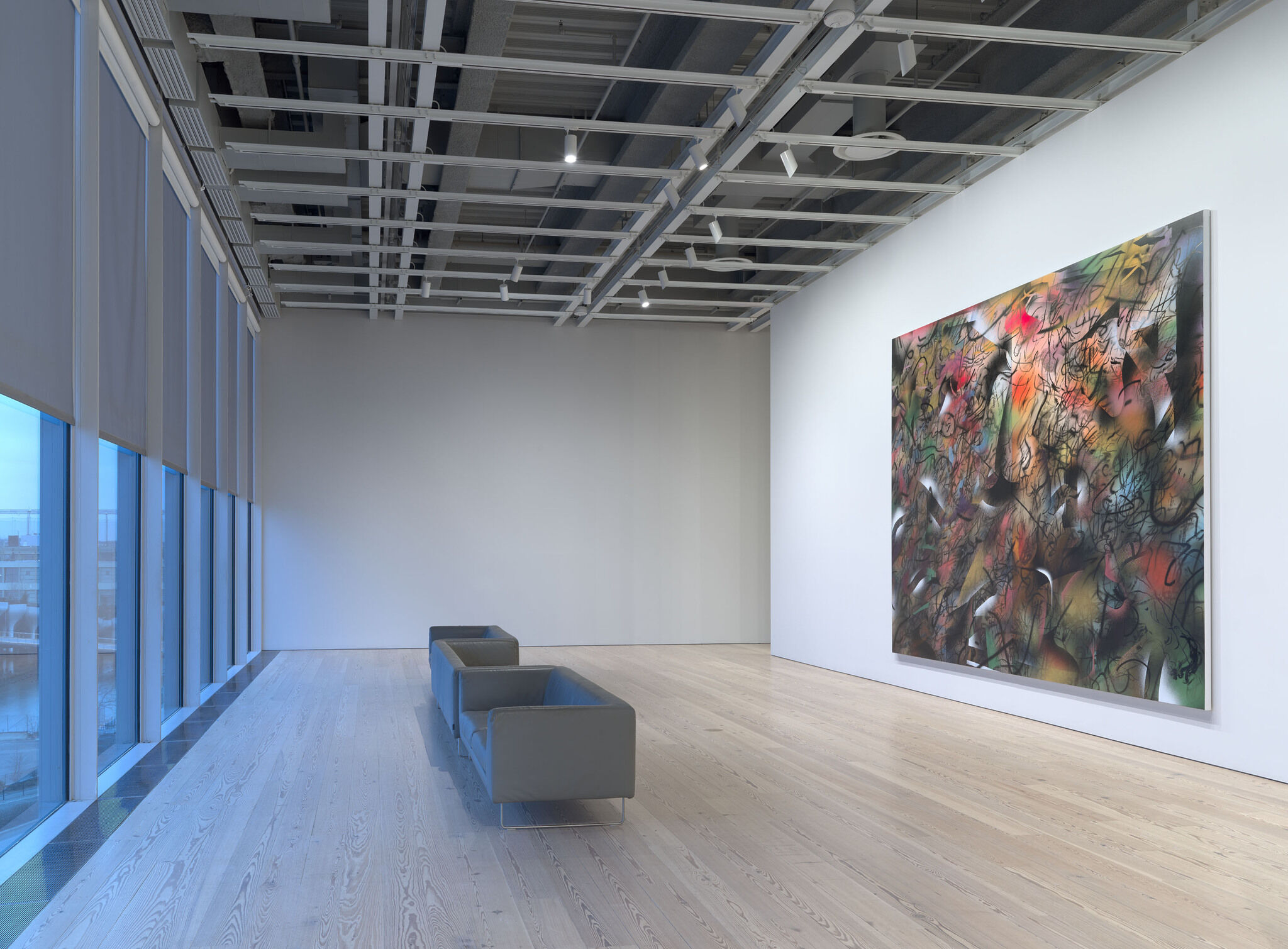 A wall of glass windows faces an exhibition wall with a large piece mounted on it. 