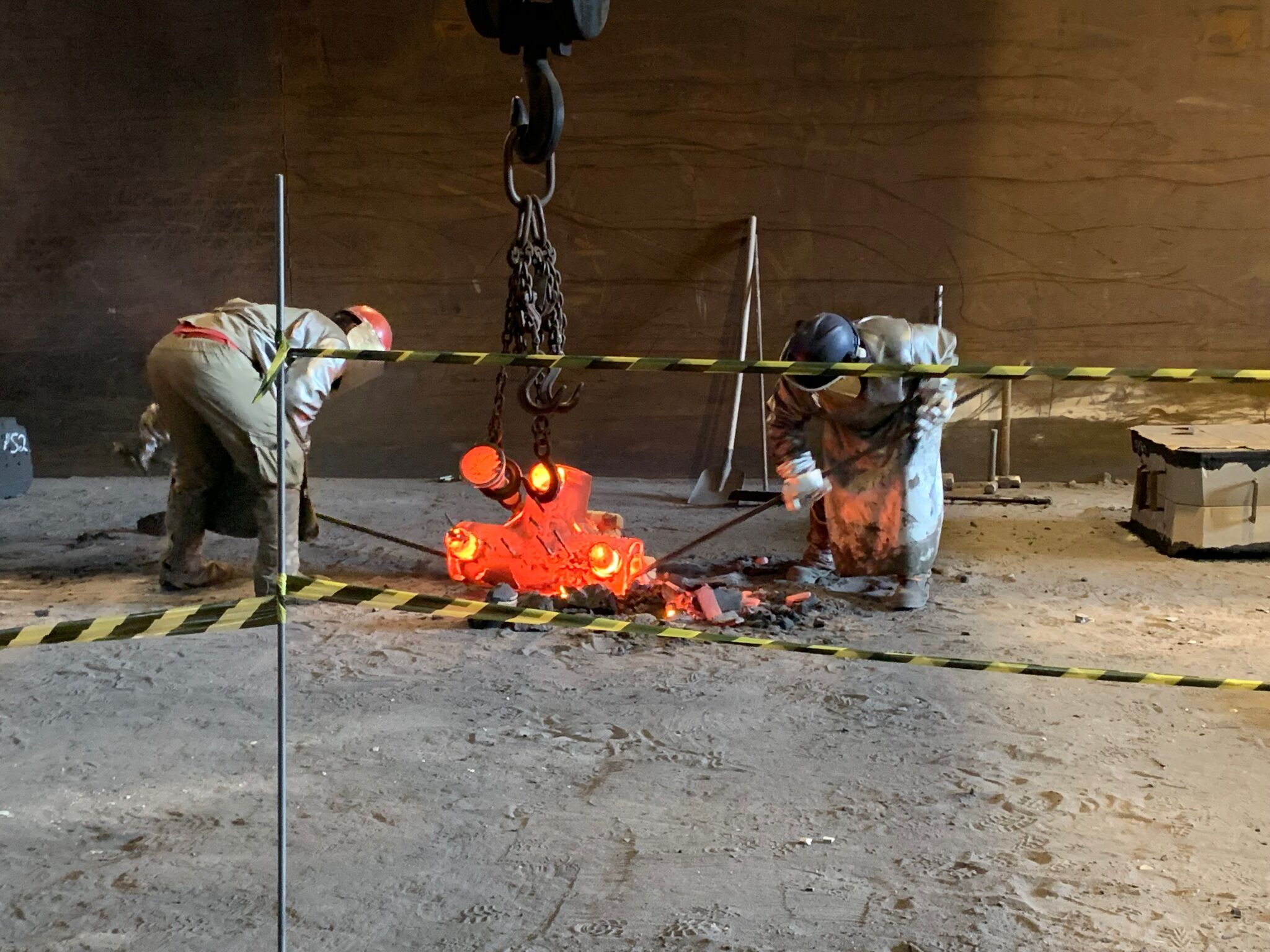 Metalworkers manipulating a large piece of red-hot steel in the fire during the casting process.