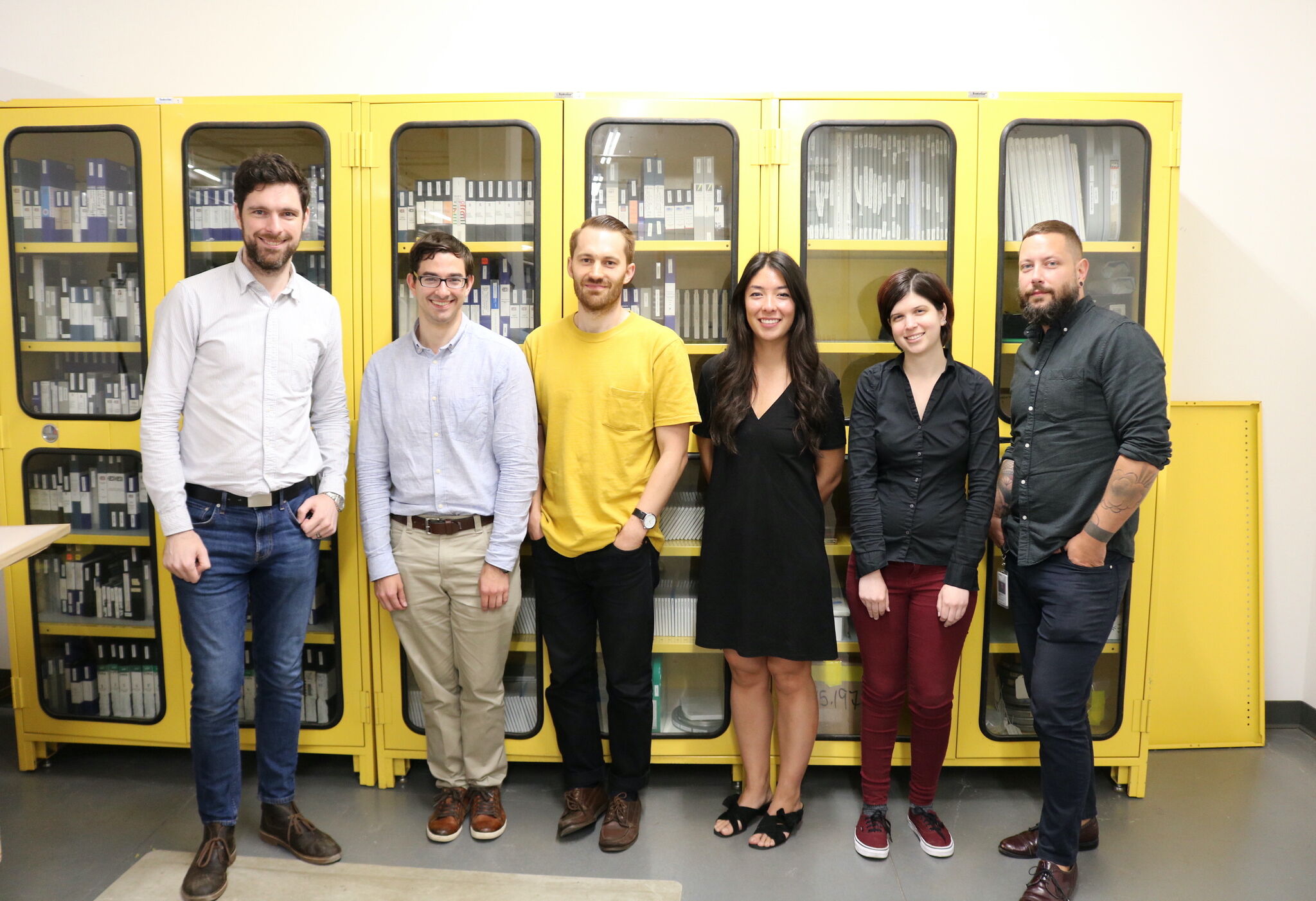 Five team members stand posed in front of a series of yellow cabinets. 