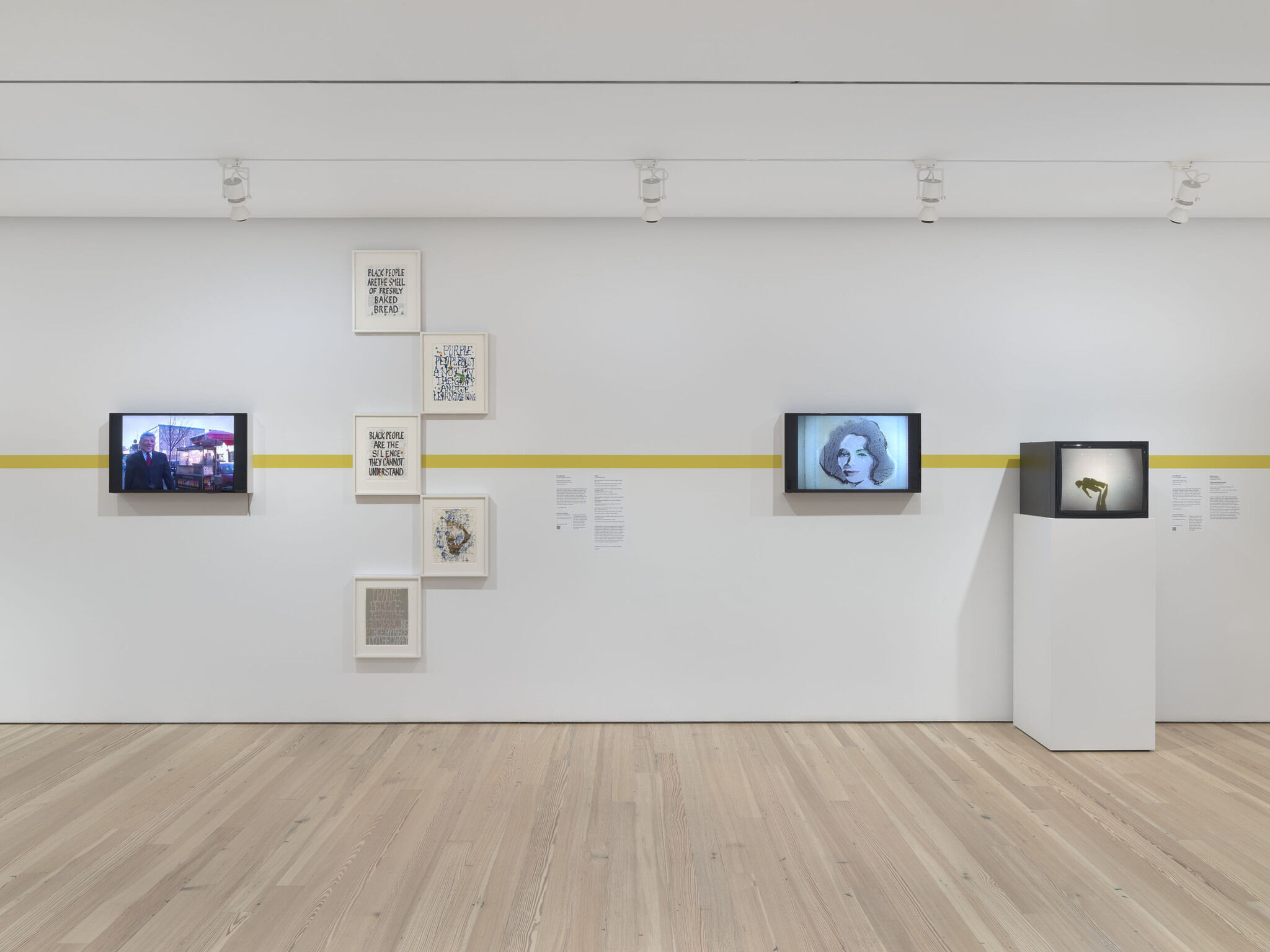 A series of black screens and framed prints are mounted against a white exhibition wall.