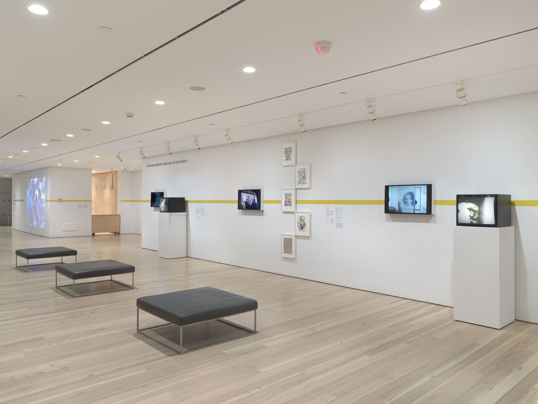 A main exhibition room featuring black monitor screens and framed, print pieces. 