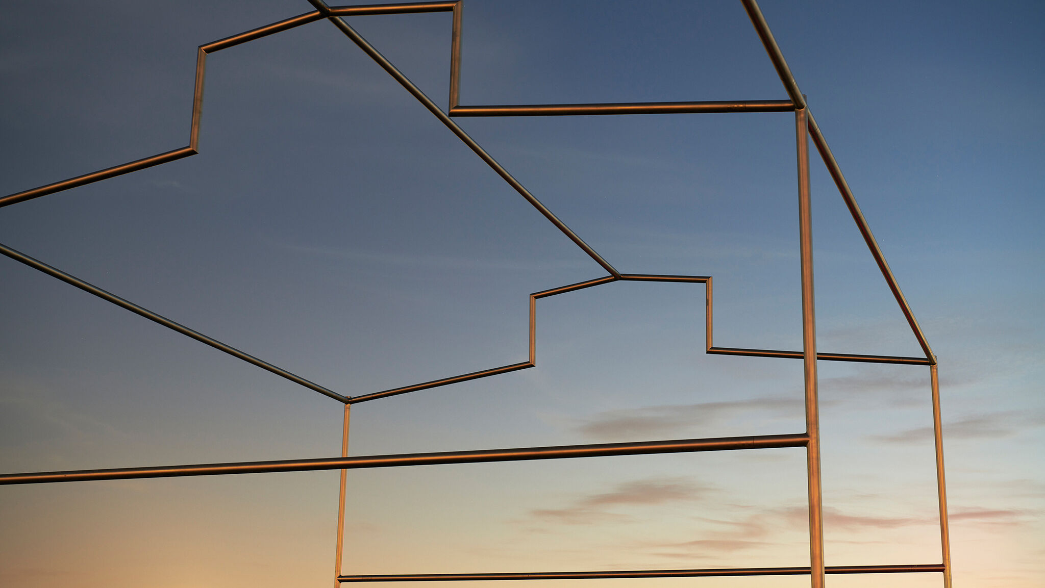 Outline of a building made from steel pipes, against a sunset sky.