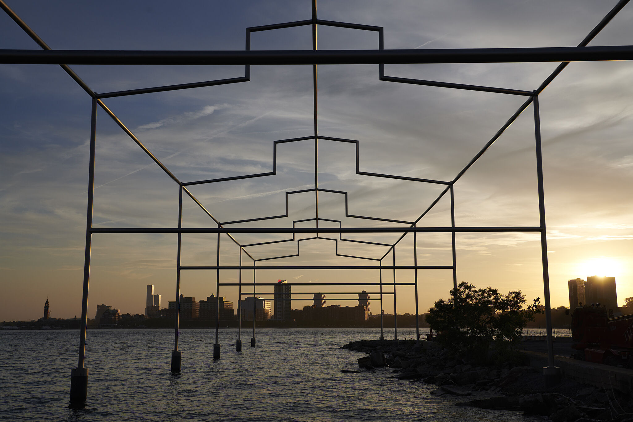 Close-up frontal view of Day's End steel sculpture, with sunset and New Jersey skyline in the background.