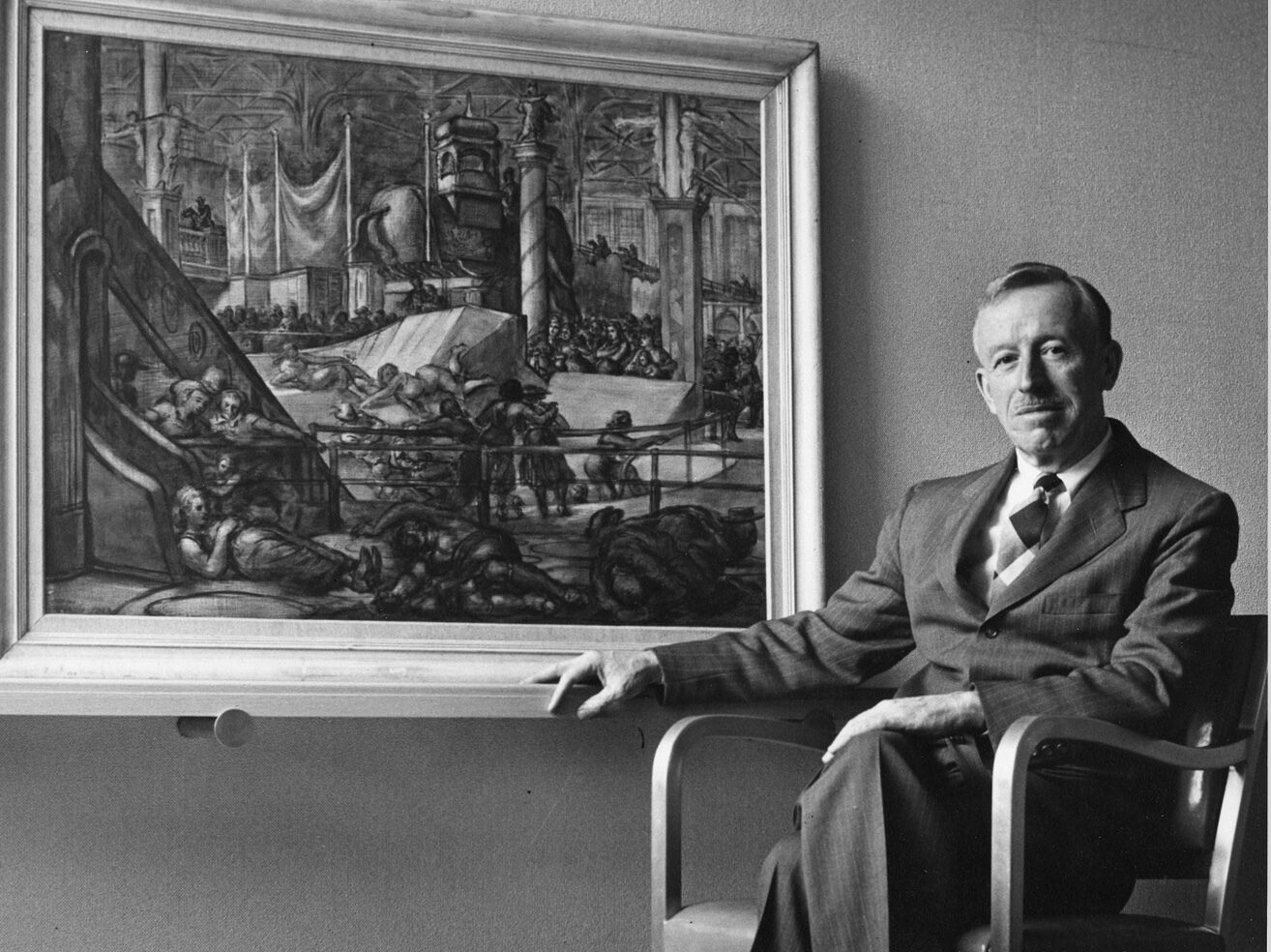 A man sits on a chair in front of a large, framed painting. 