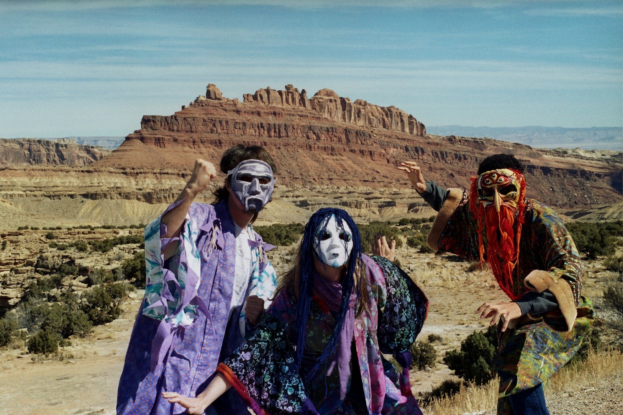 Three masked people in front of a desert landscape.