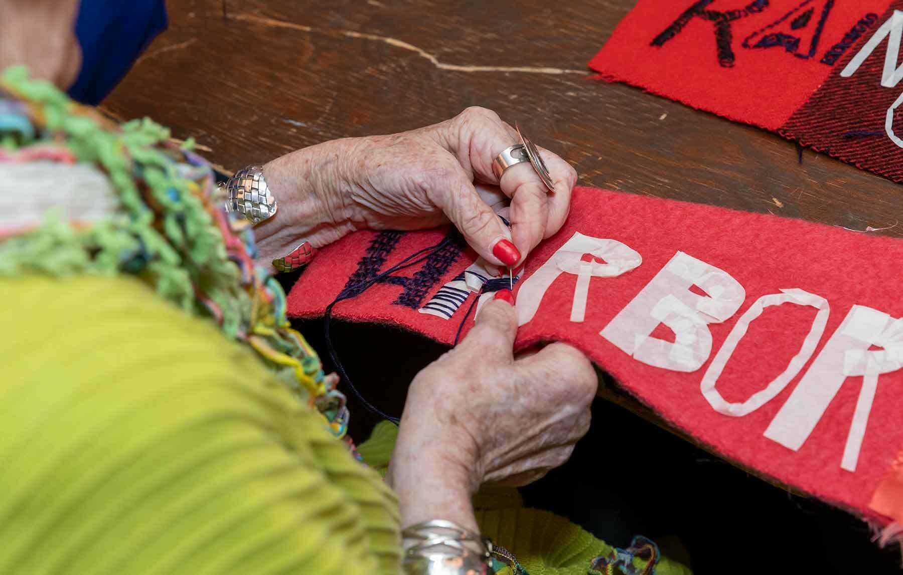 Hands stitching words on a banner.