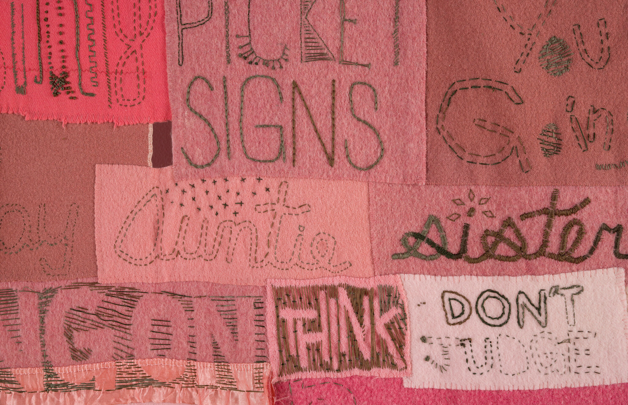Rectangles of varying shades of pink fabric, stitched with words.