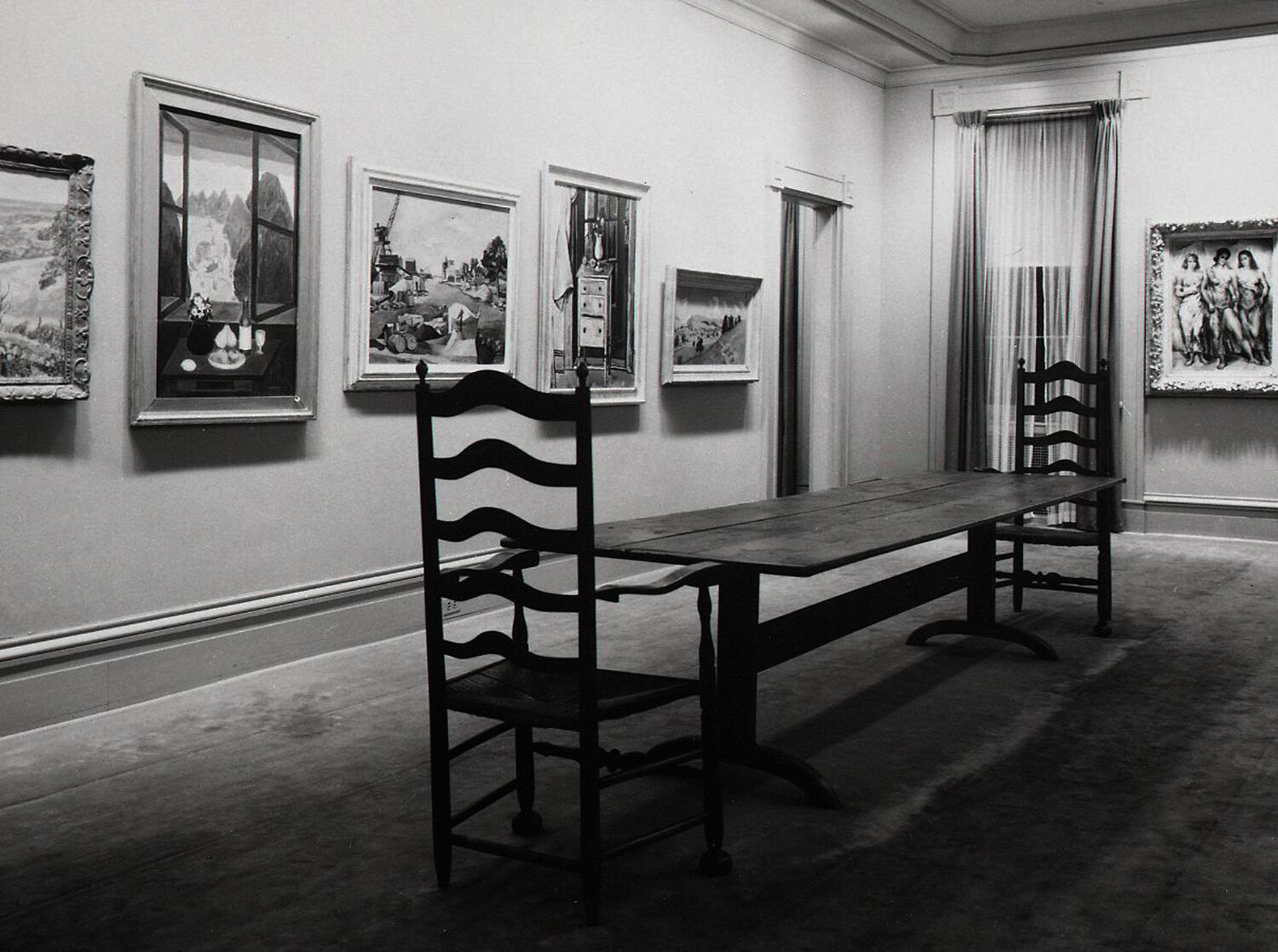 Black-and-white photograph of paintings hanging in a dining room.