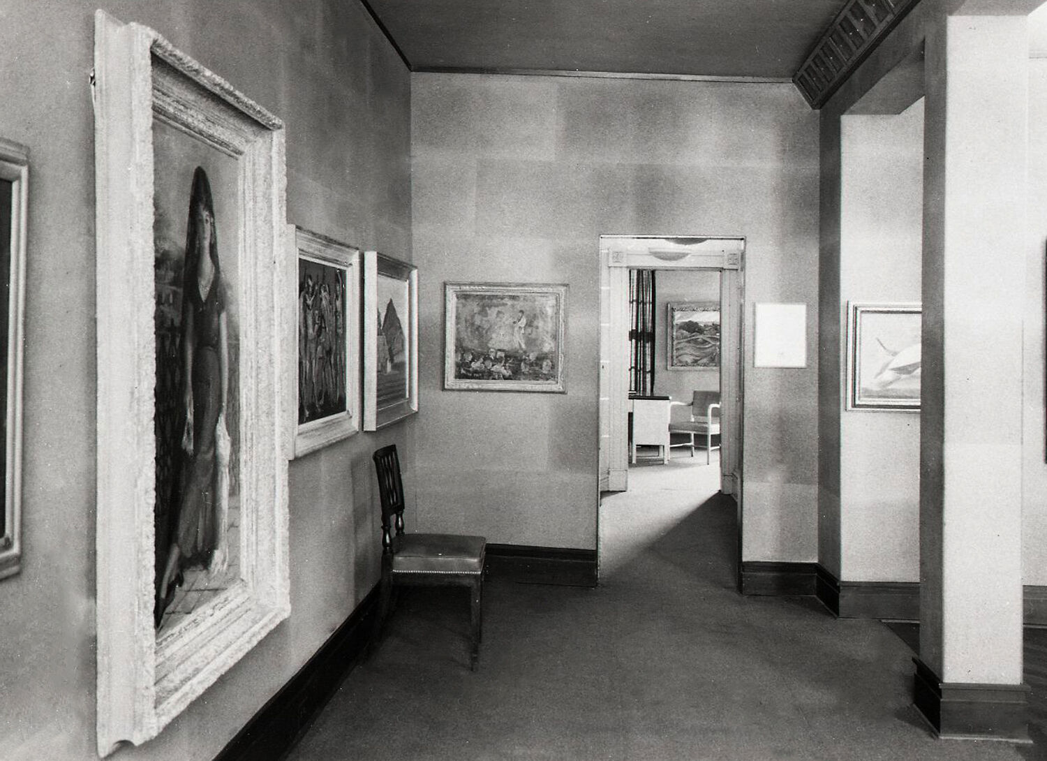 Black-and-white photograph of paintings hanging in a hallway.