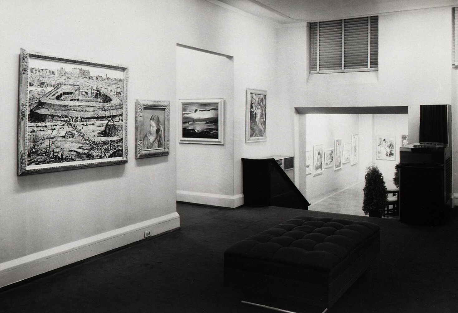 Black-and-white photograph of paintings hanging in a hallway at the top of stairs.