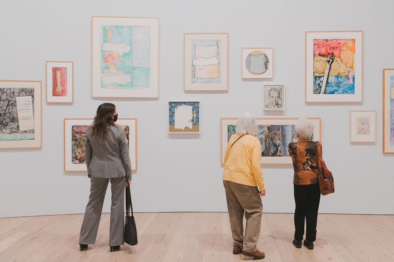 Three people stand in front of an exhibition wall for Jasper Johns: Mind/Mirror.