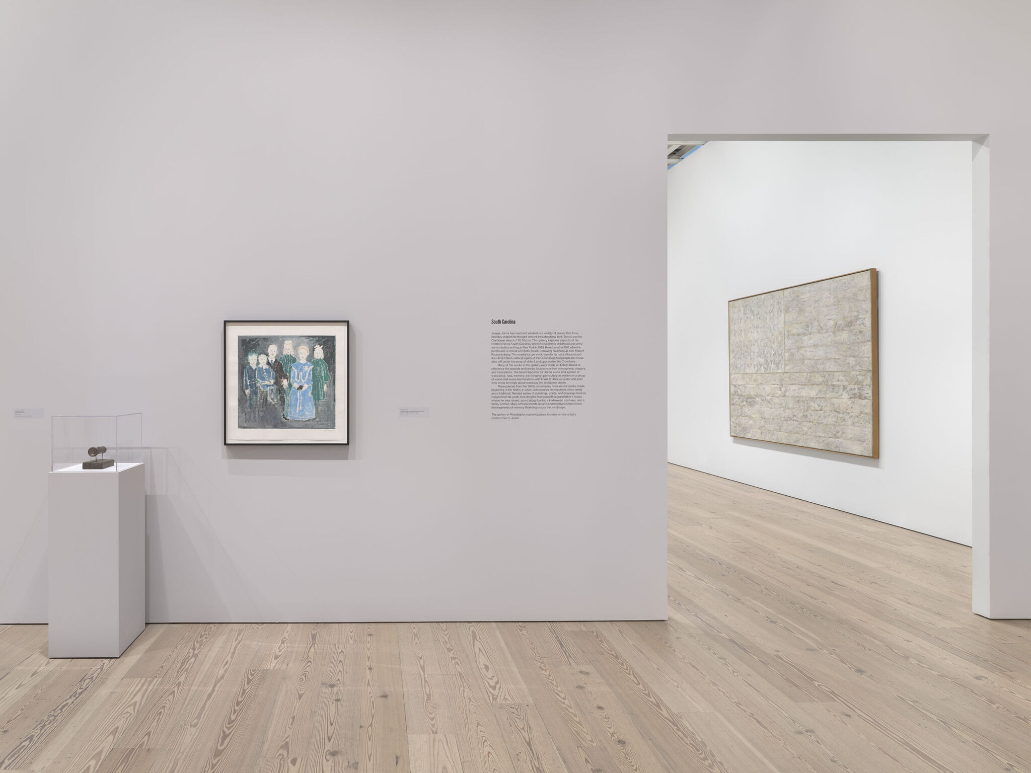 A white exhibition room with two framed works and a third work encased in glass. 