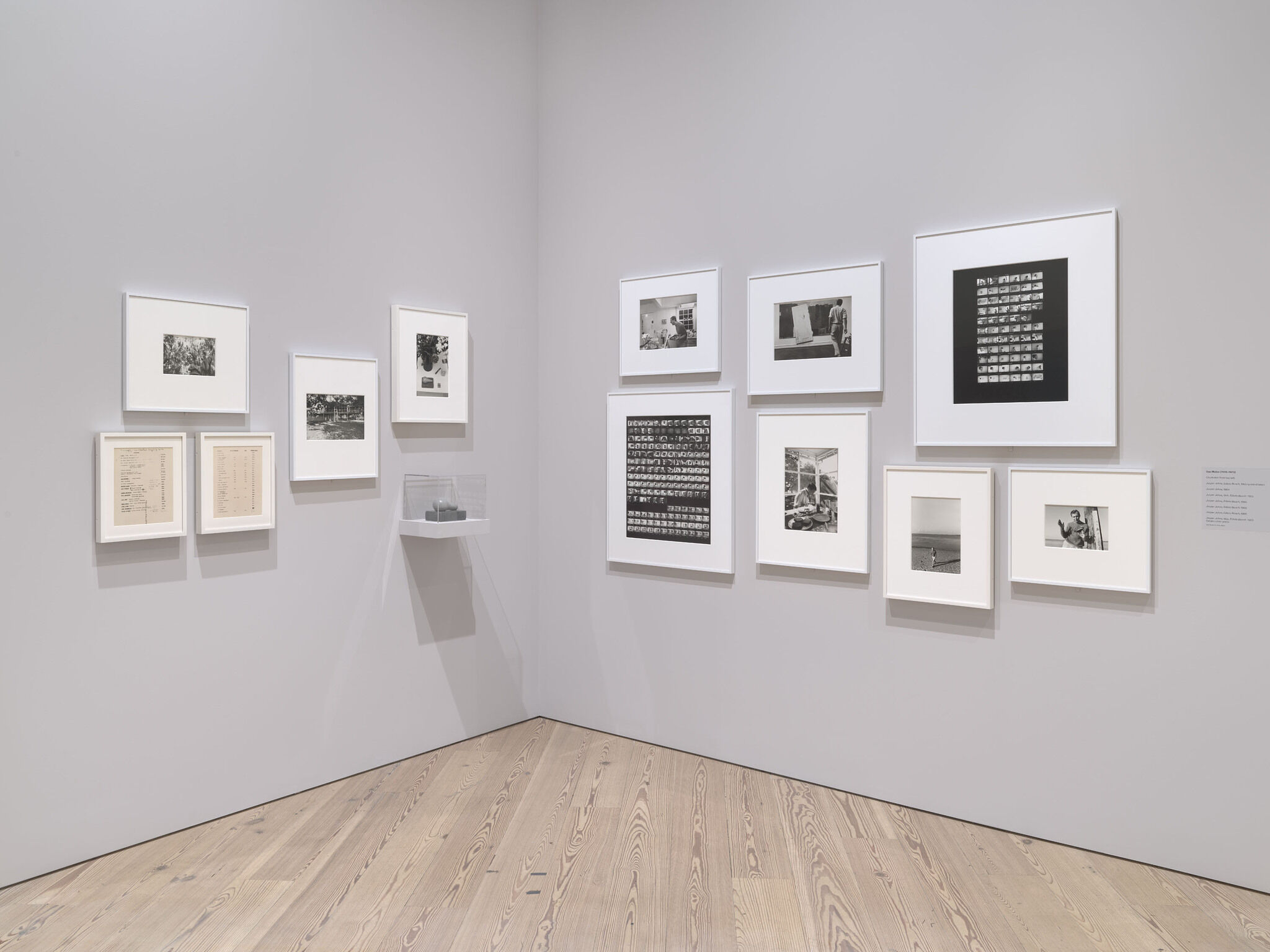 A white exhibition wall with thirteen works mounted next to each other.