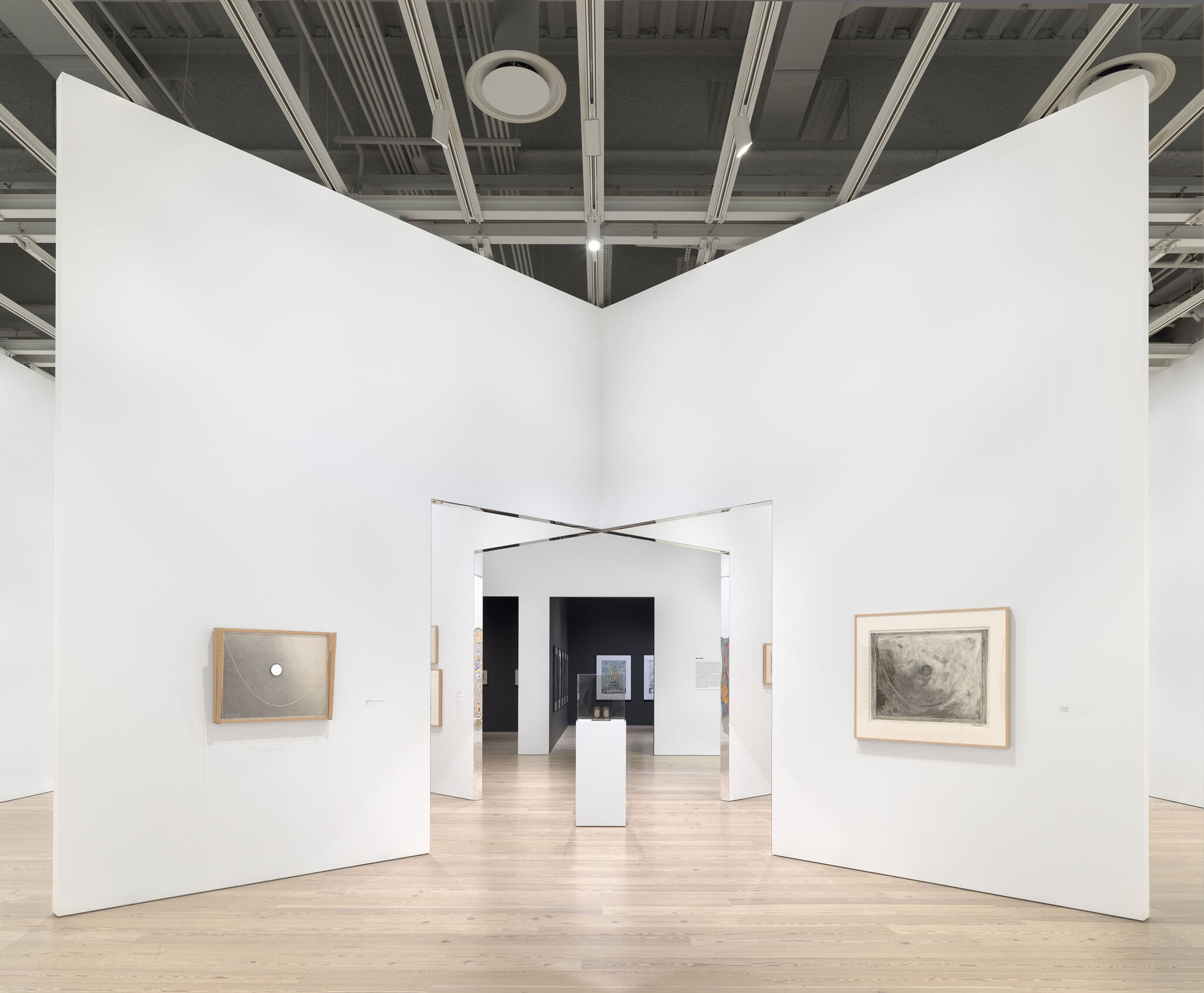 A white exhibition room with two intersecting walls at its center and works mounted on each side. 