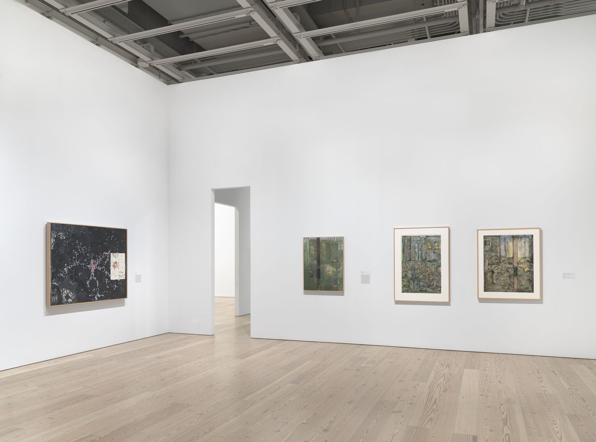 A white exhibition wall with four works mounted next to each other. 