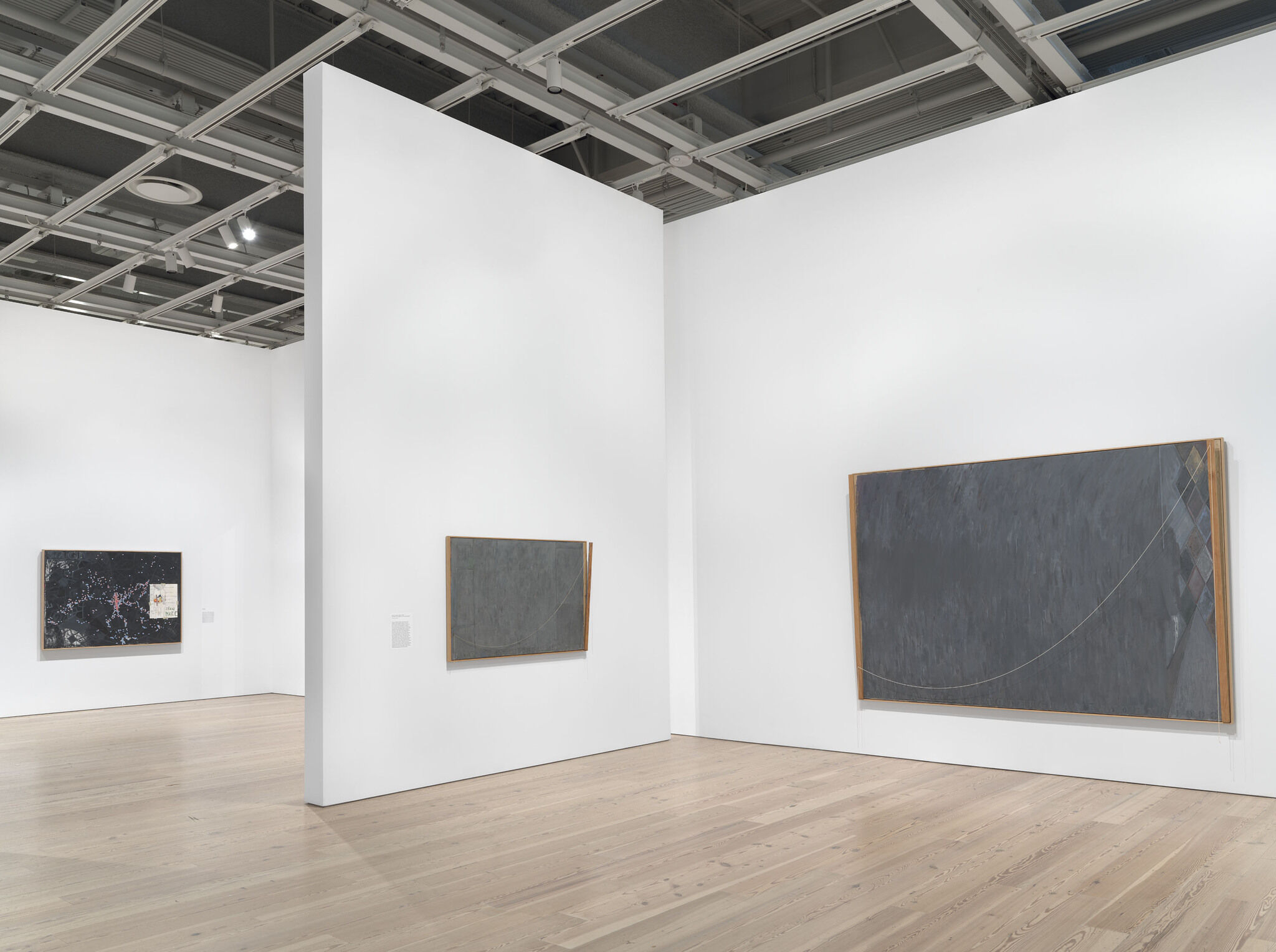 A white exhibition room with three works mounted across three separate walls. 